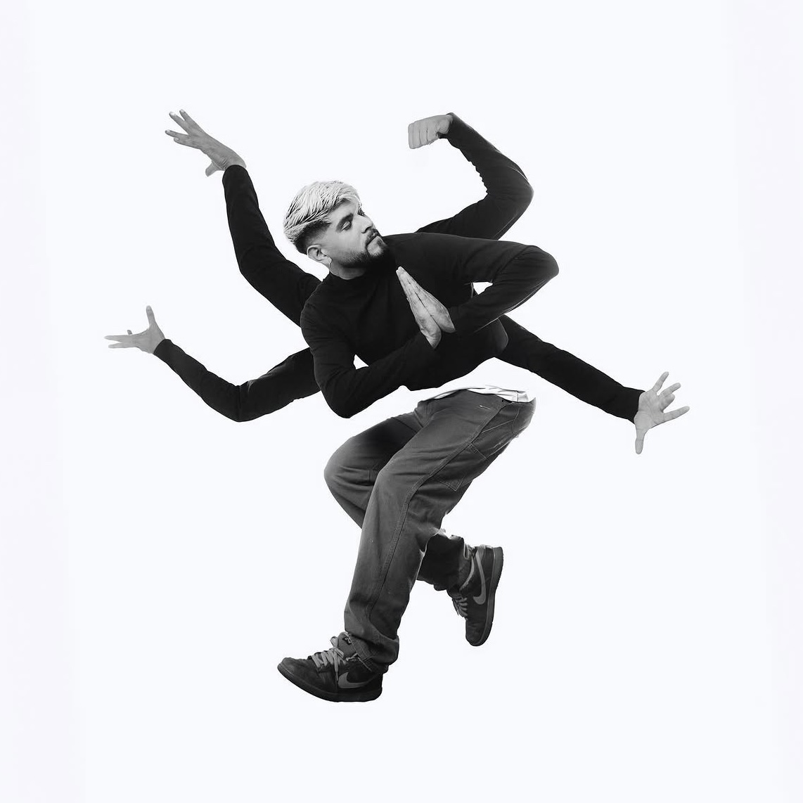 Person with multiple arms in a dance pose, wearing dark clothing and pants, against a plain background.