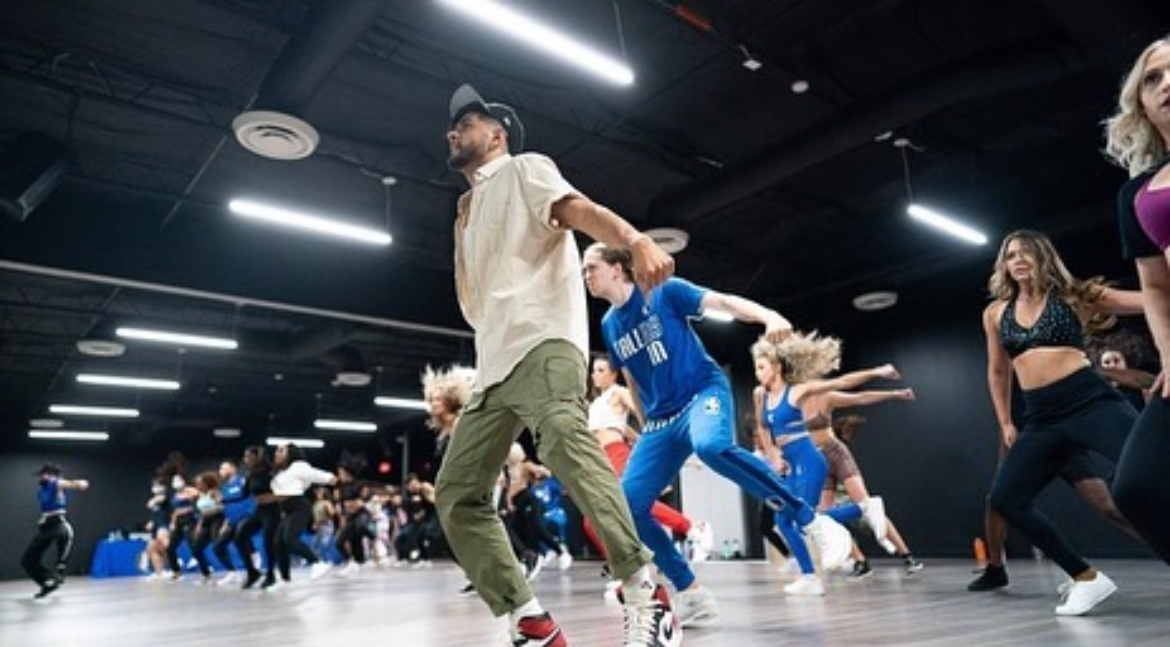 Group of people dancing in a large indoor space with black ceiling and bright overhead lights.