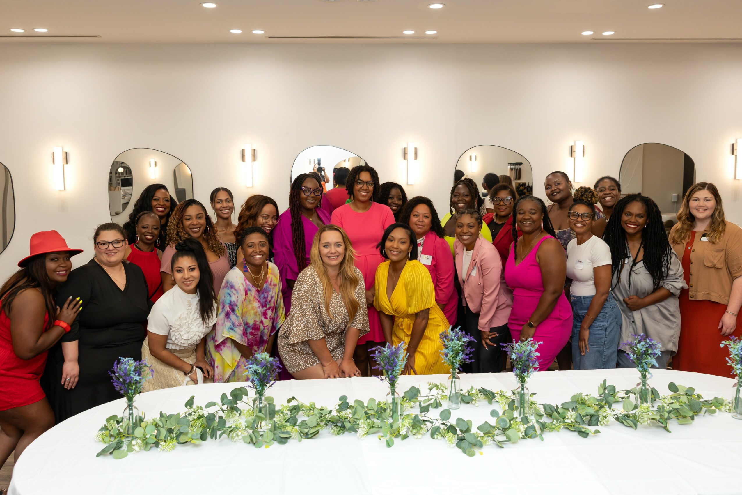 Group of women and girls standing behind a decorated table in a room with mirrors and wall lights.
