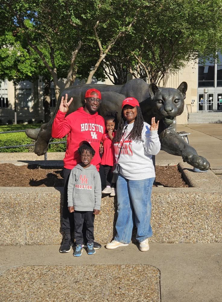 Three people standing in front of a panther statue outdoors, making peace signs, with trees and buildings in the background.