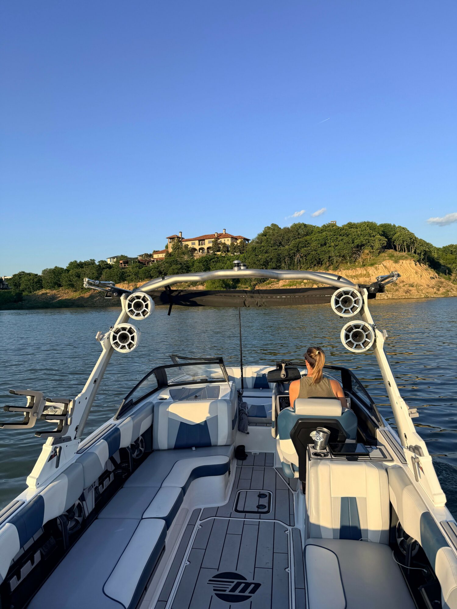 View from a boat showing the deck, steering wheel, and water with a shoreline and trees in the background.