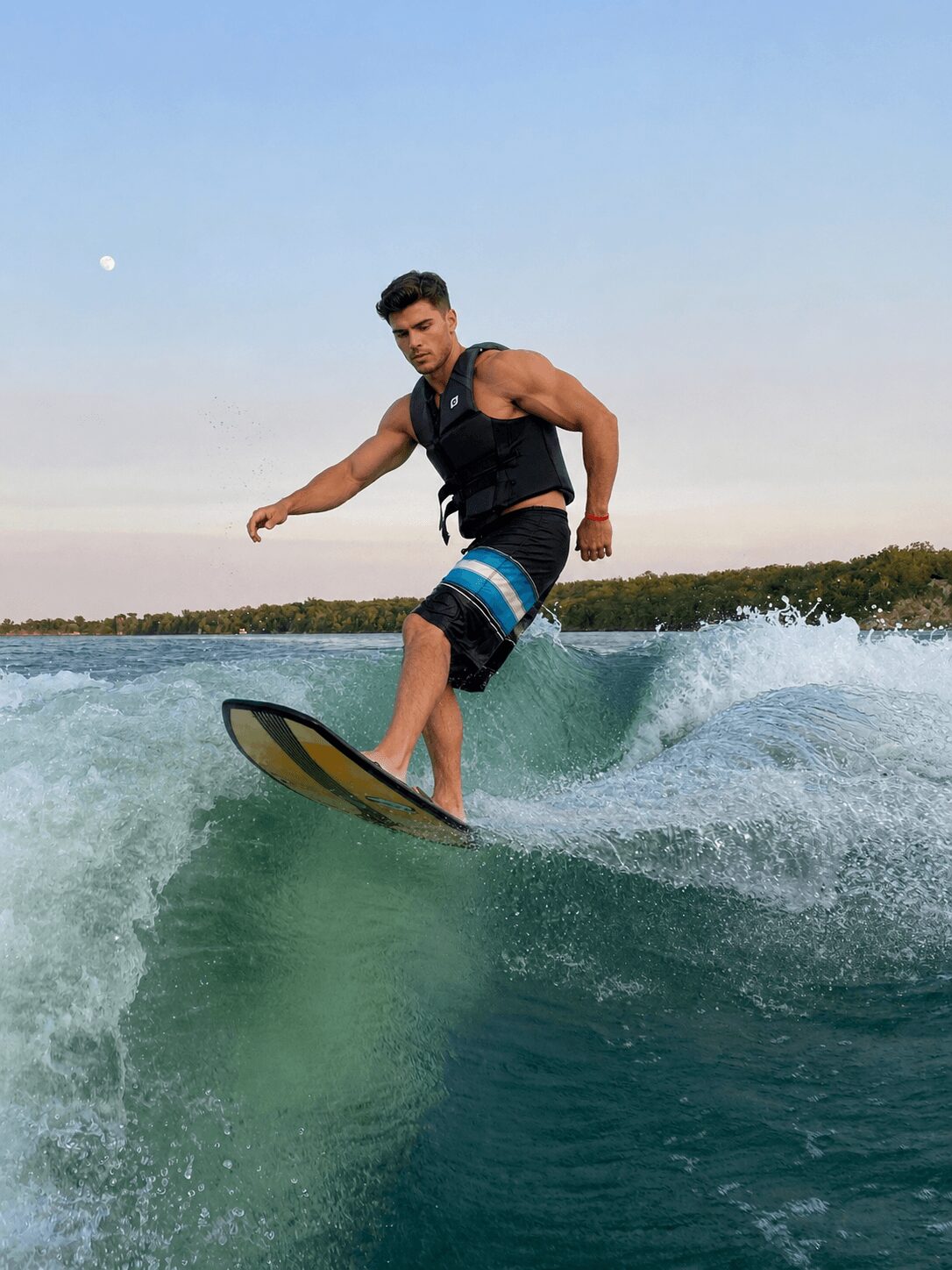 Person surfing on a wave with a clear sky and distant trees in the background.