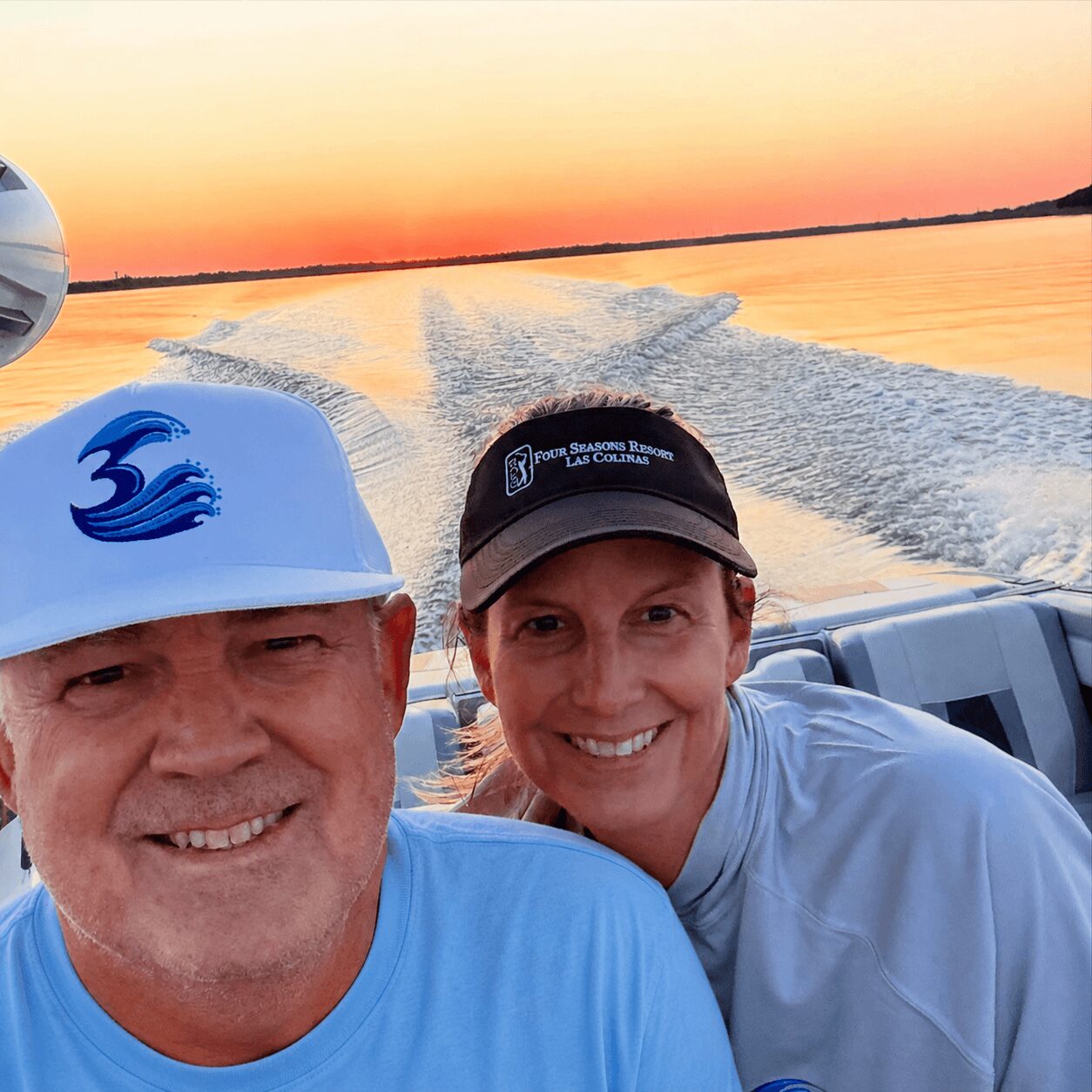 Two people smiling on a boat at sunset with water and sky in the background.