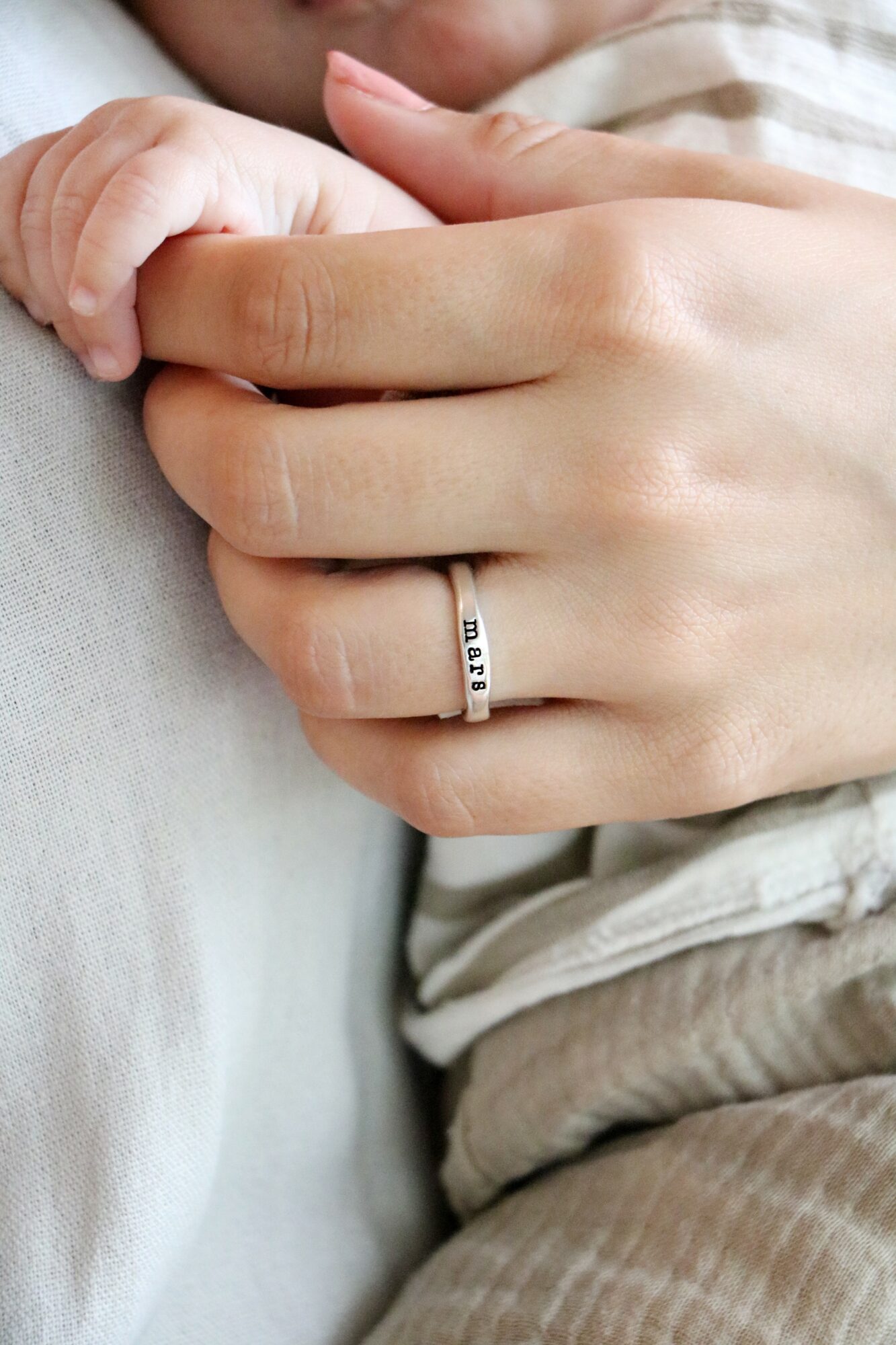Close-up of a person's hand with a ring, holding a child's hand, both resting on a soft surface.