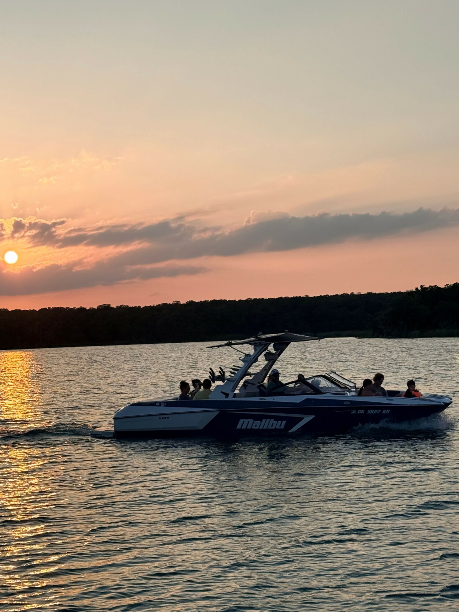Boat on water during sunset with a pink and orange sky, trees in the background, and calm water reflections.