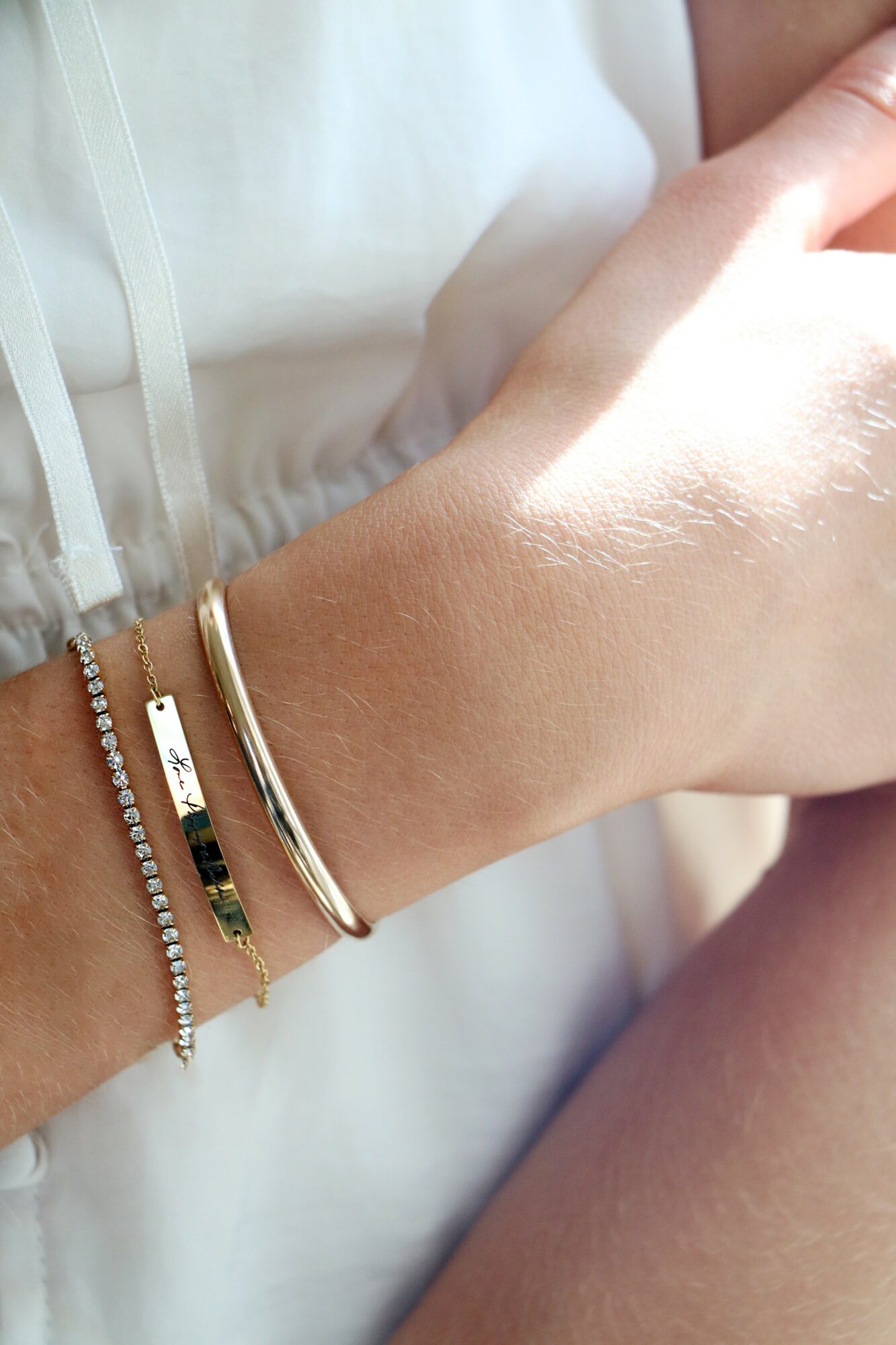 Close-up of a person's wrist with multiple bracelets, wearing a white top, with sunlight reflecting on the skin.