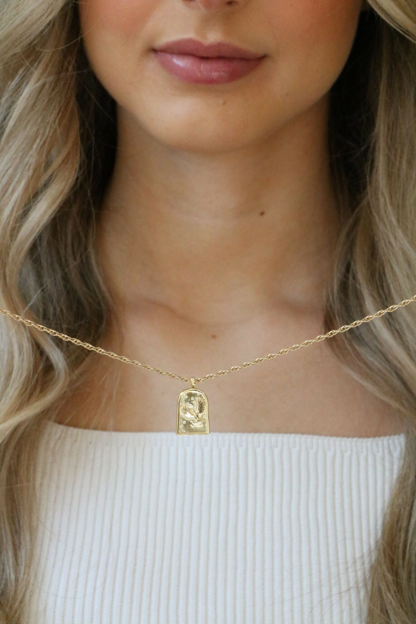 Close-up of a woman's face and neck, showing lips, part of white top, and a gold necklace.