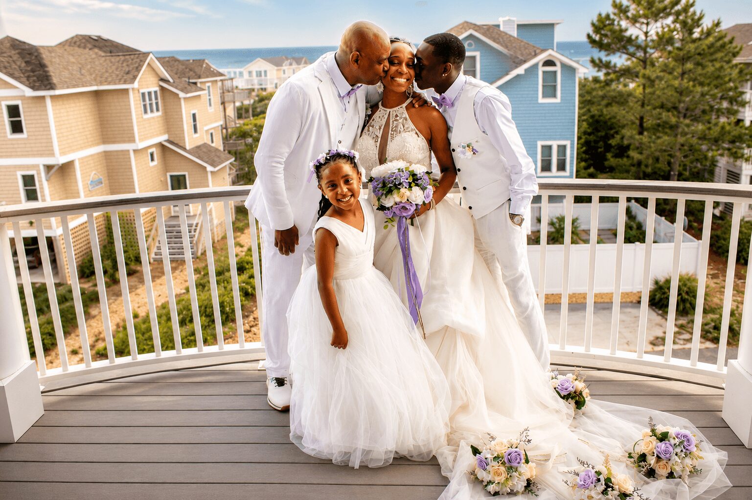 Family celebrating wedding on balcony, with houses and trees in background, all smiling and dressed in white and pastel colors.
