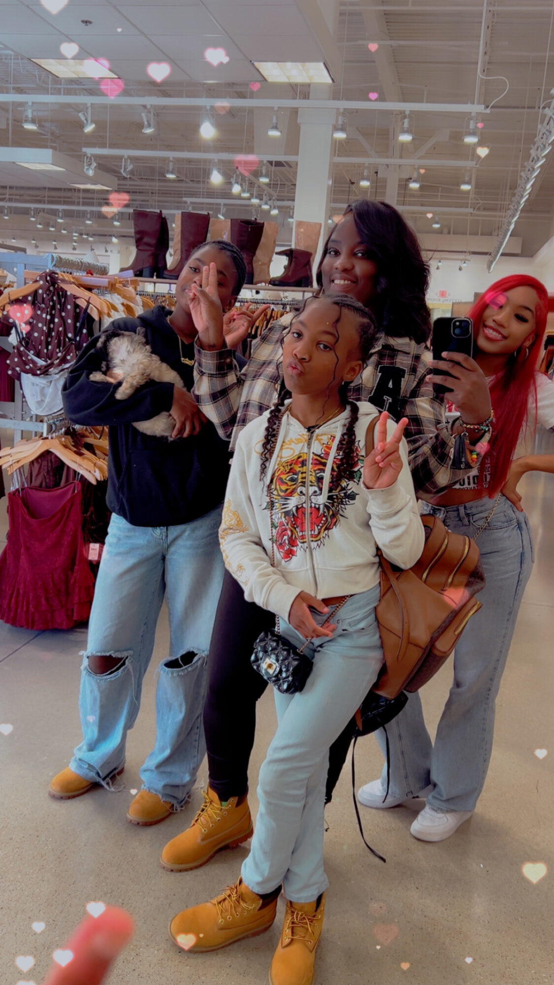 Four women posing in a store, with clothing racks and shelves in the background, some making peace signs and smiling.