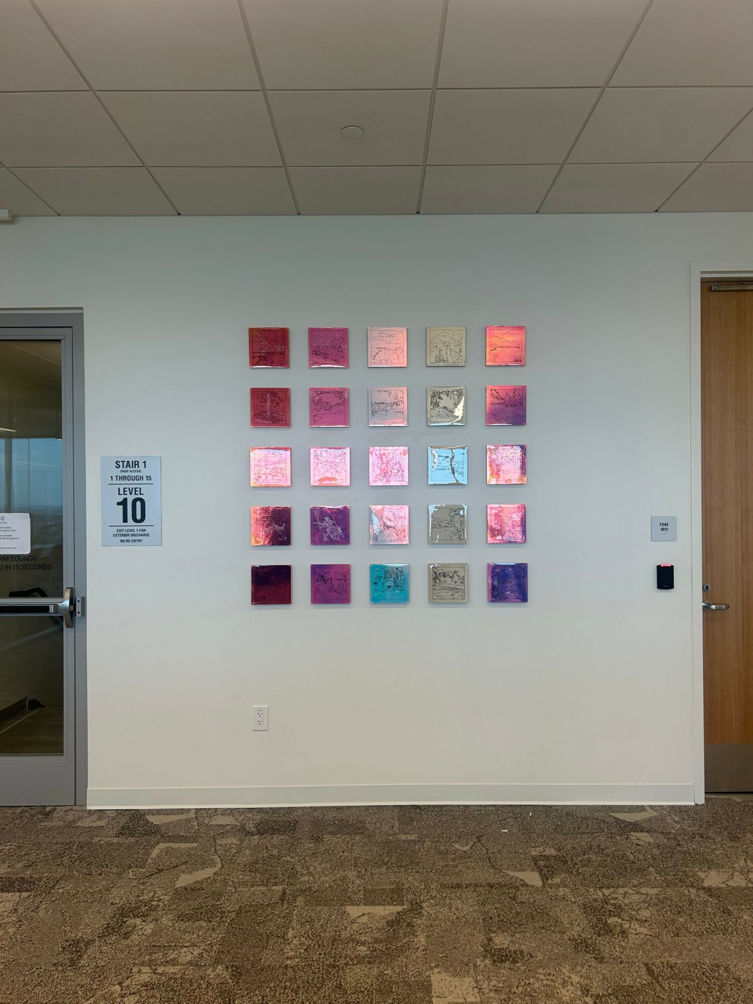 White wall with colorful square panels arranged in a grid, a sign with text, and a small device at the top.
