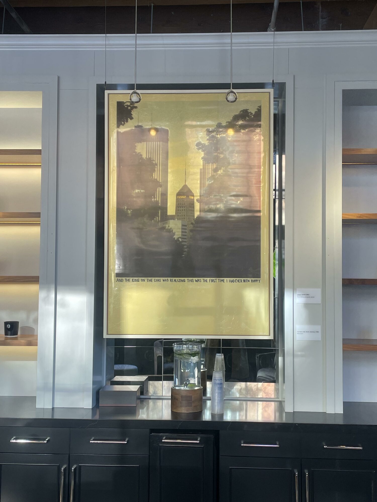 A framed poster of a city skyline with tall buildings, hanging on a wall with metallic panels, above a counter with bottles and containers.
