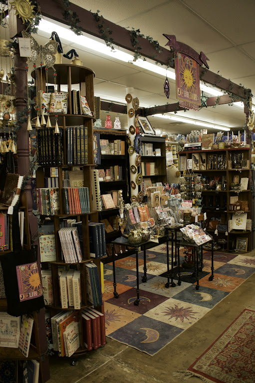 Bookshelves filled with books and decorative items in a bookstore, with tables displaying small items and a colorful rug on the floor.