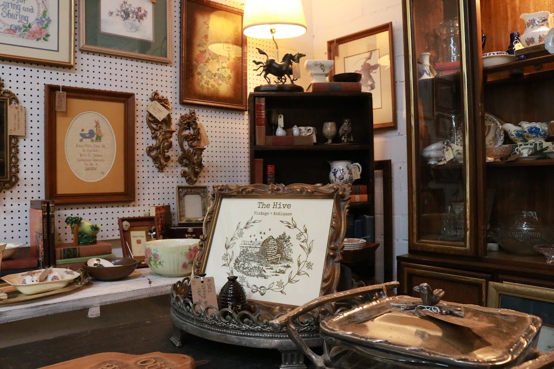 Interior of a room with antique furniture, framed artwork, and decorative items on shelves and tables.