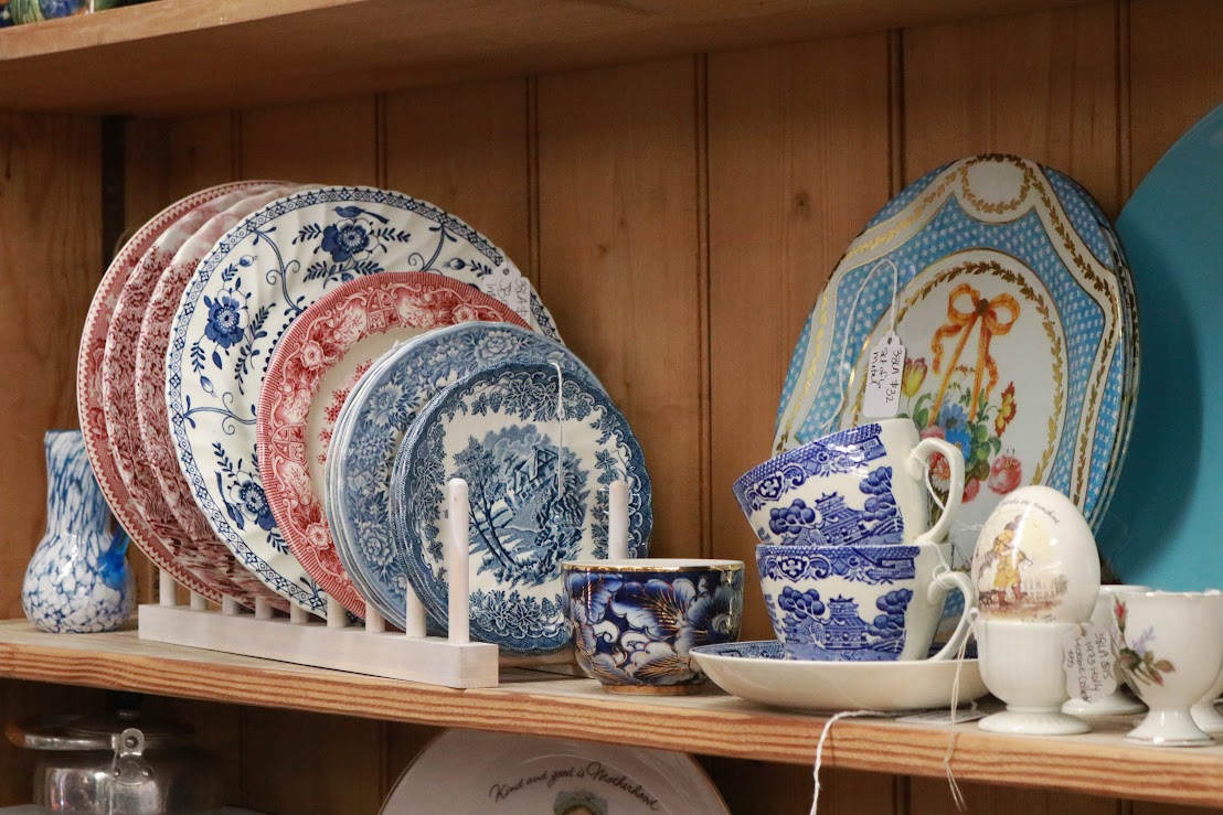 Stacked decorative plates and cups on a wooden shelf, with a wooden wall background.