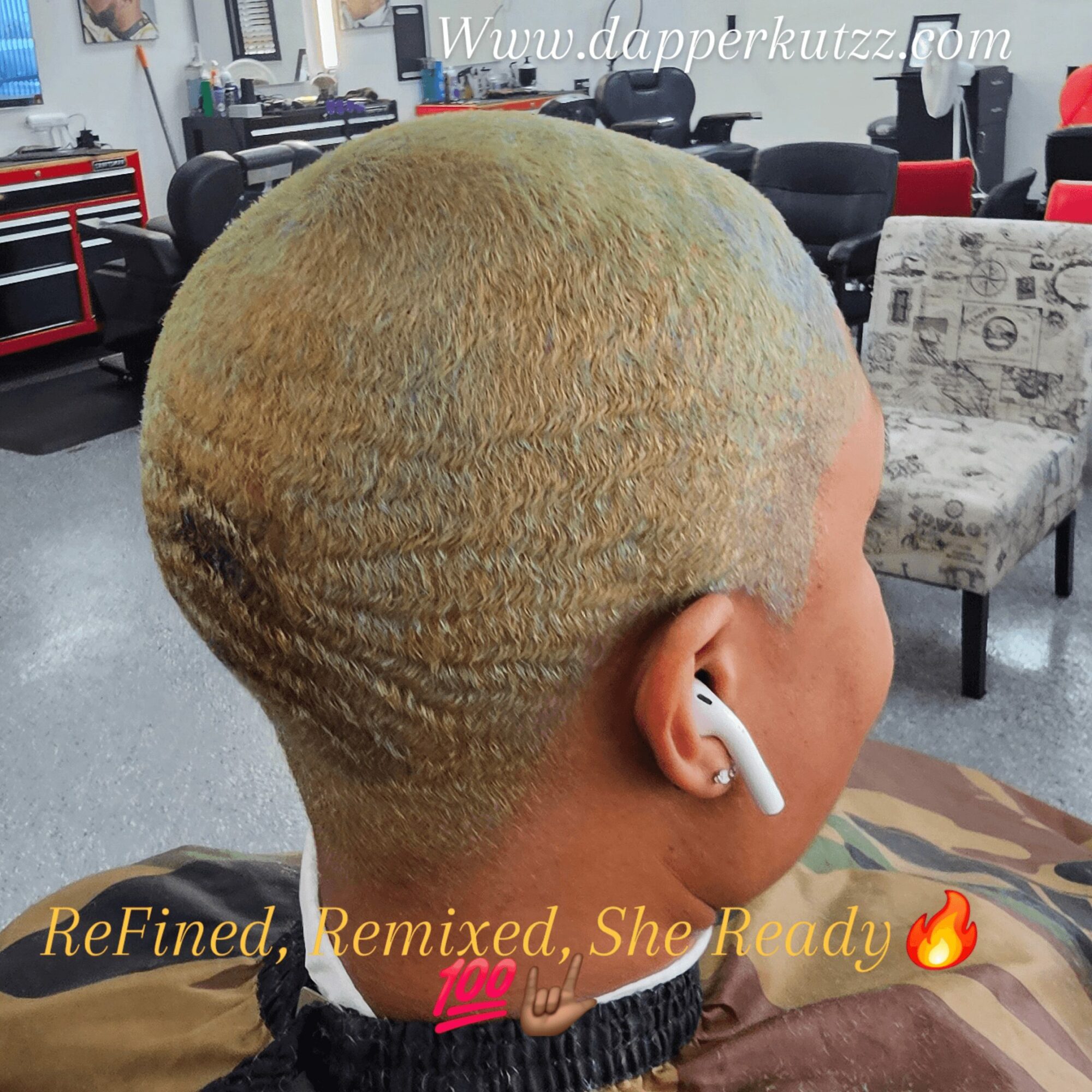 Person with short, blonde, textured hair wearing wireless earbud in a salon or barbershop. Background includes chairs and tools.