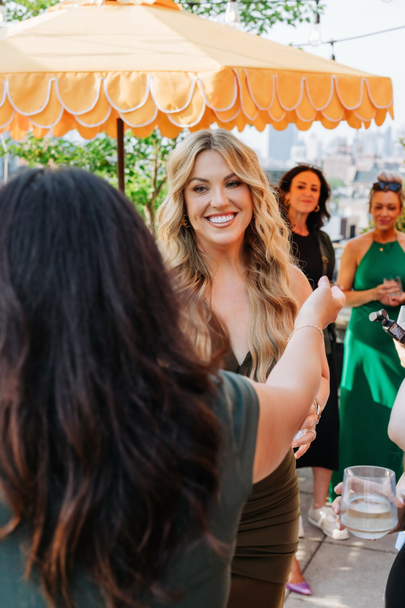 Group of women socializing outdoors under a yellow umbrella, smiling and engaging in conversation.