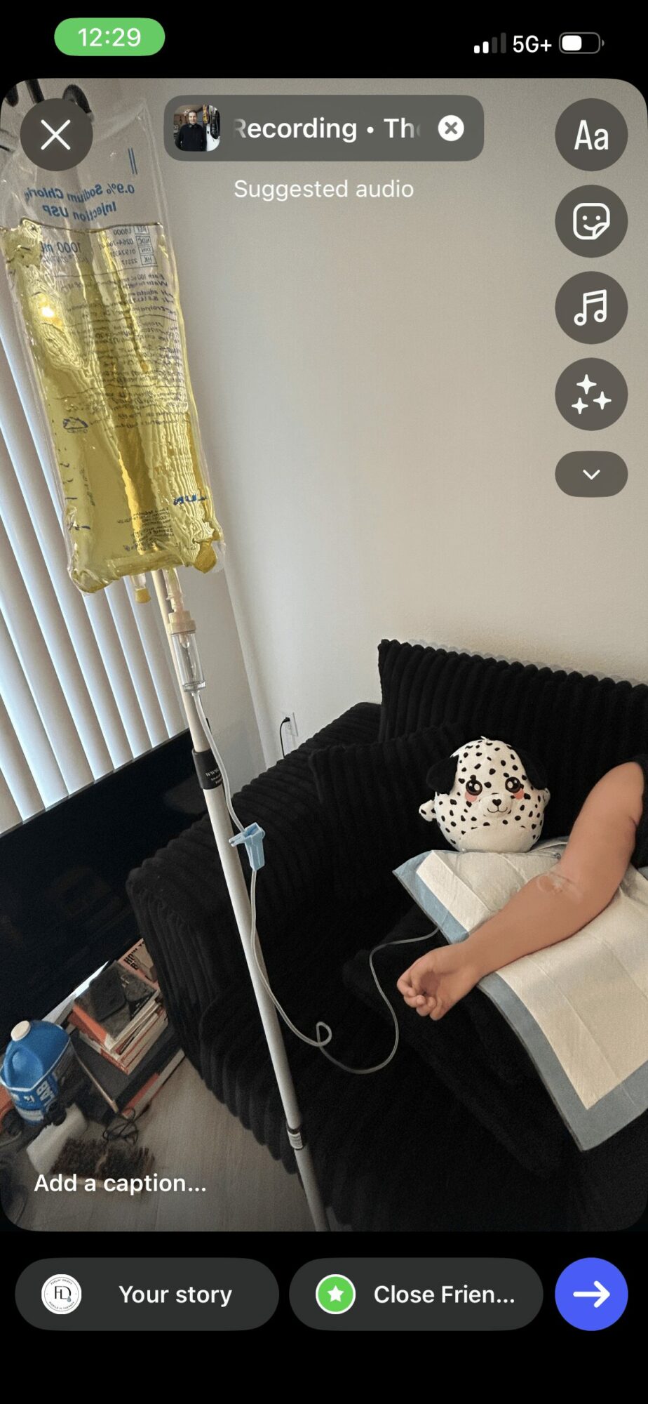 Person lying on black sofa with a white blanket, a stuffed animal, and a pillow, in a room with a window and curtain.