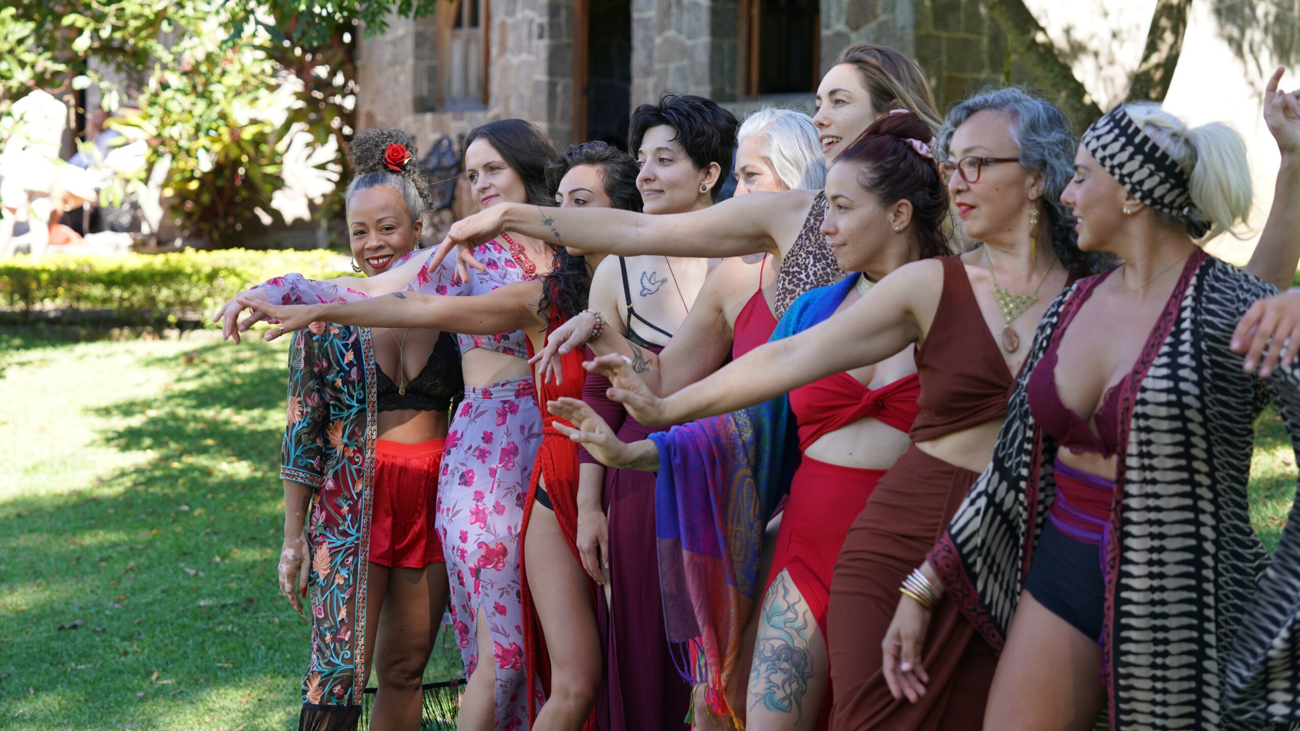 Group of women standing outdoors, stretching their arms forward, in a park with trees and grass.