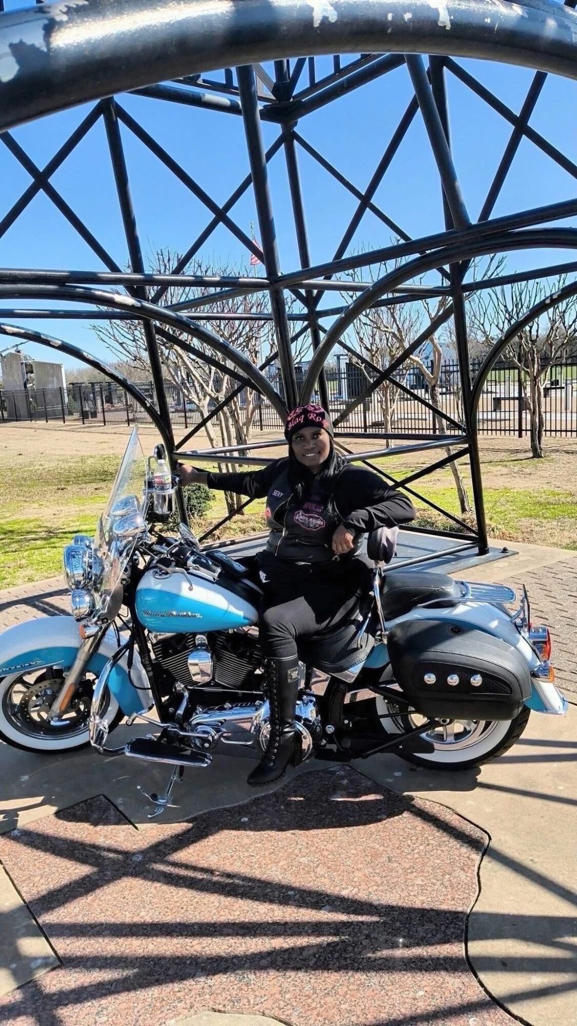 Person sitting on a blue motorcycle under a large metal structure with a clear blue sky.