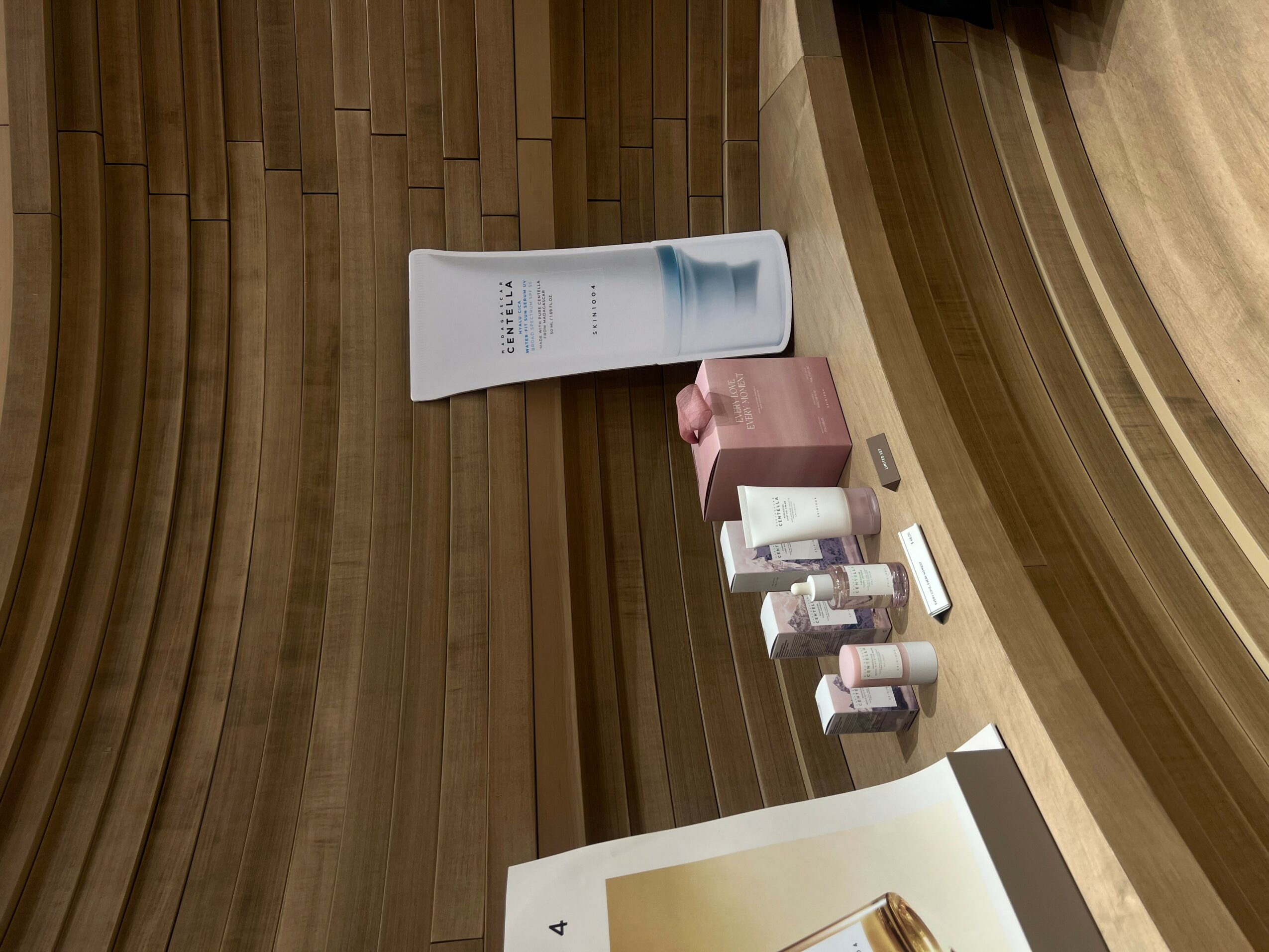 Various skincare products and a booklet on a wooden surface, with a curved wooden background.