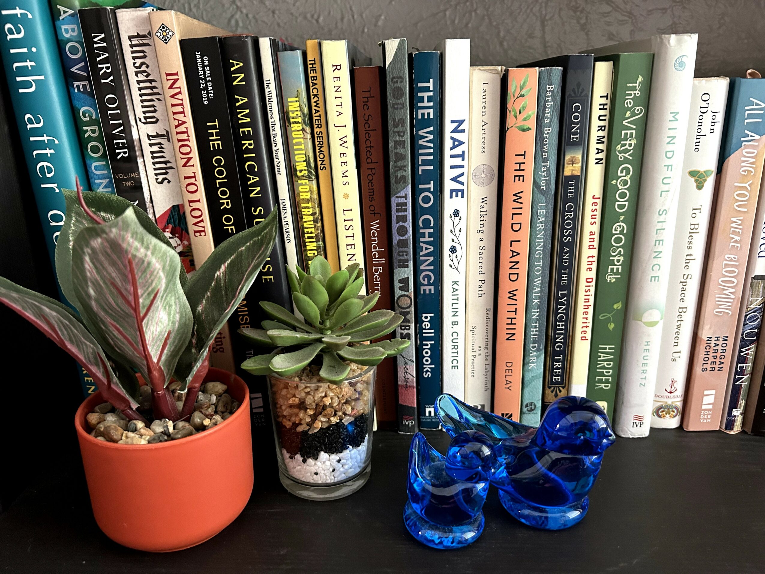 Books on a shelf with potted plants and a blue glass sculpture in front.