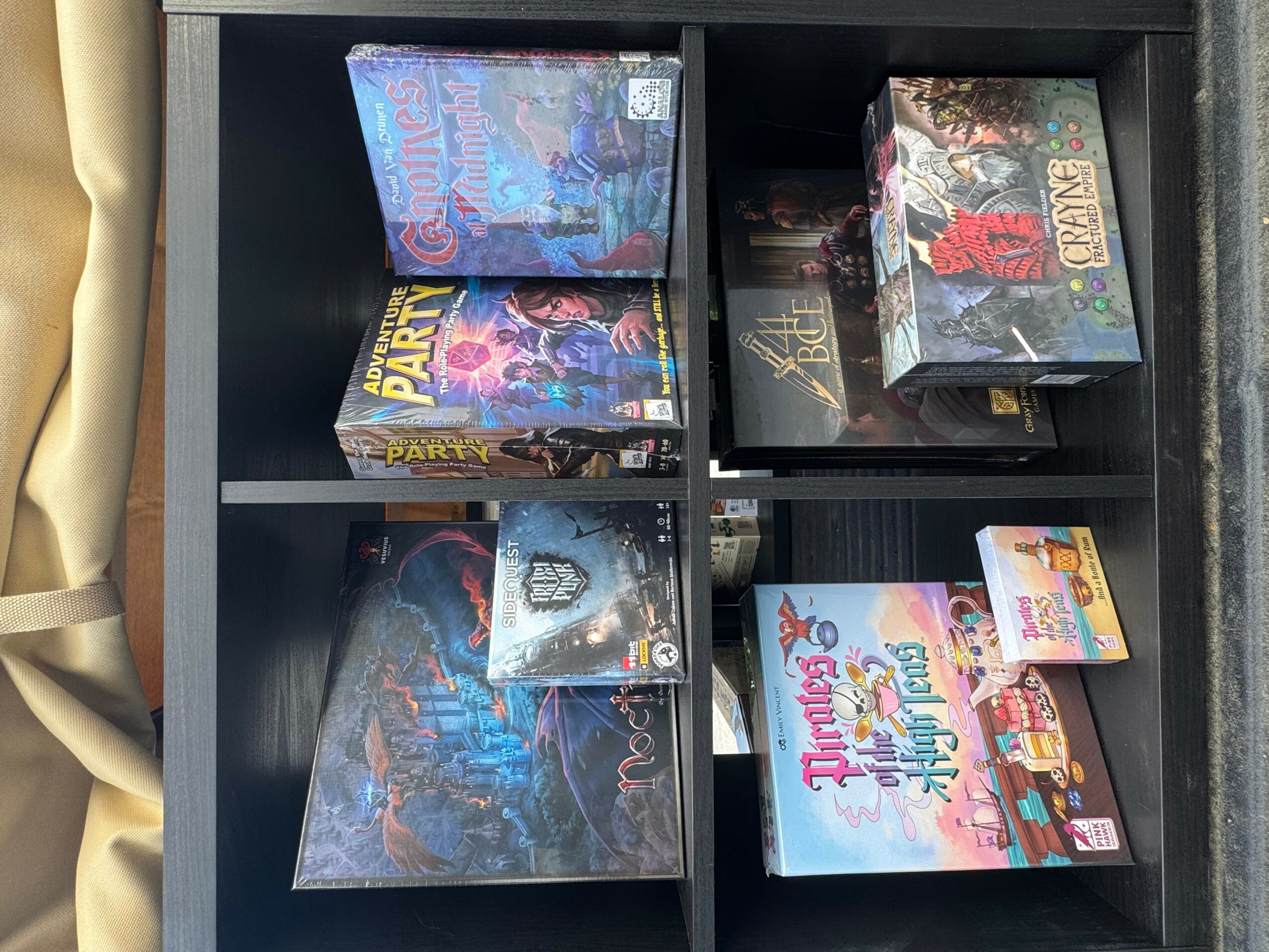 Black shelf with boxed toys and games, some with colorful packaging, arranged in compartments.