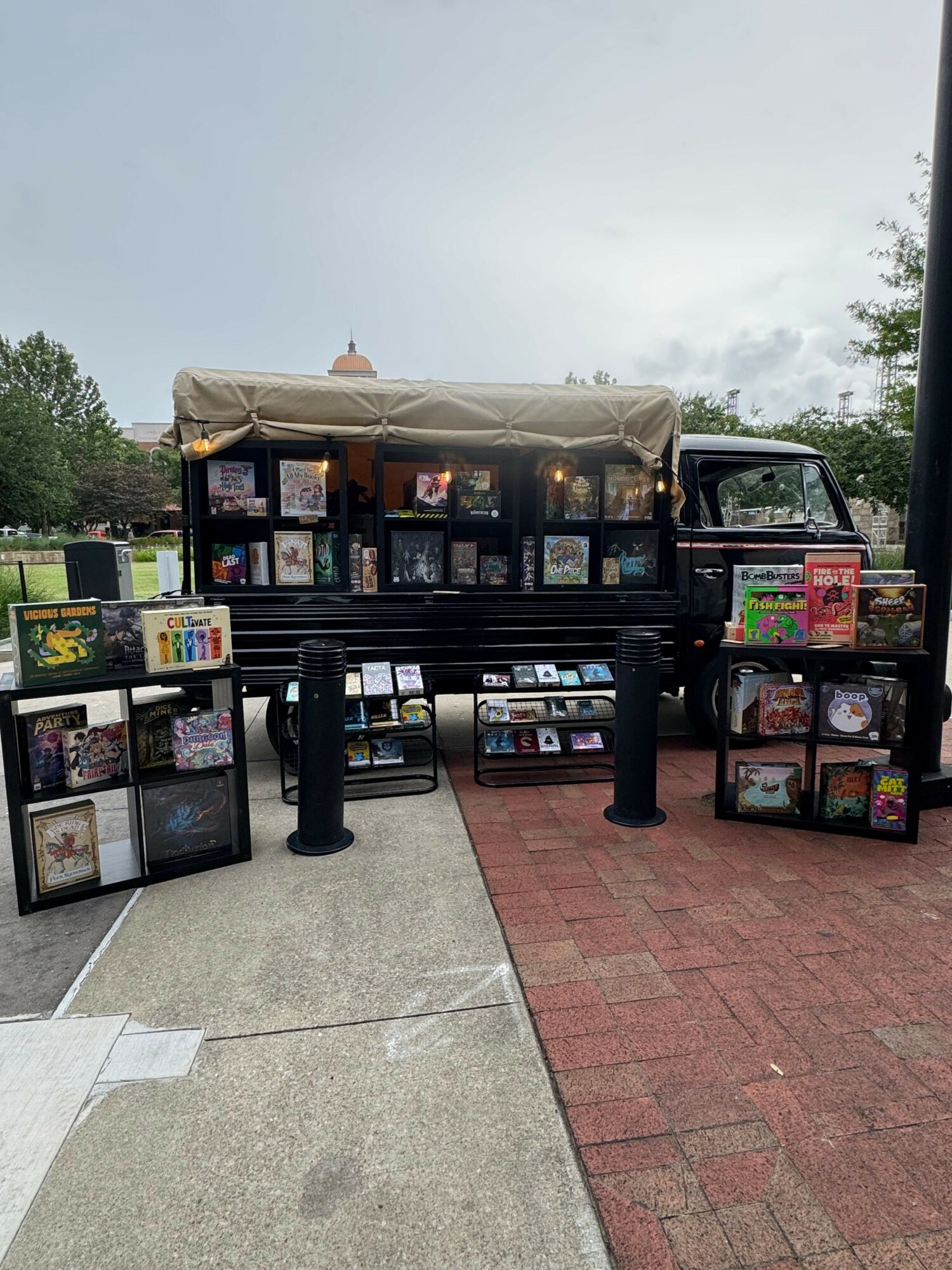 Vending cart with snacks and drinks on sidewalk, overcast sky, trees in background, brick and concrete pavement.
