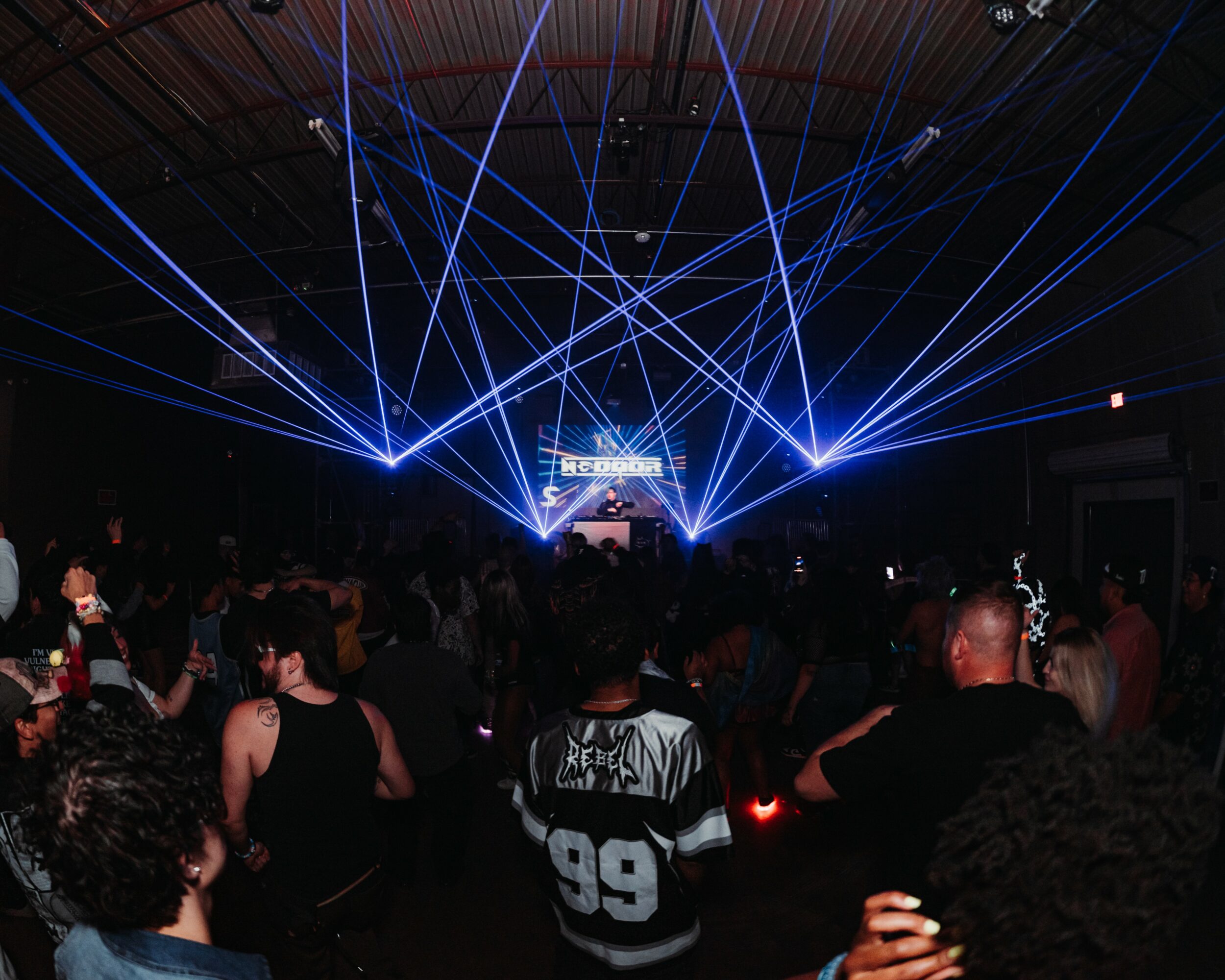 Crowd watching a concert with blue laser lights and a stage in the background.