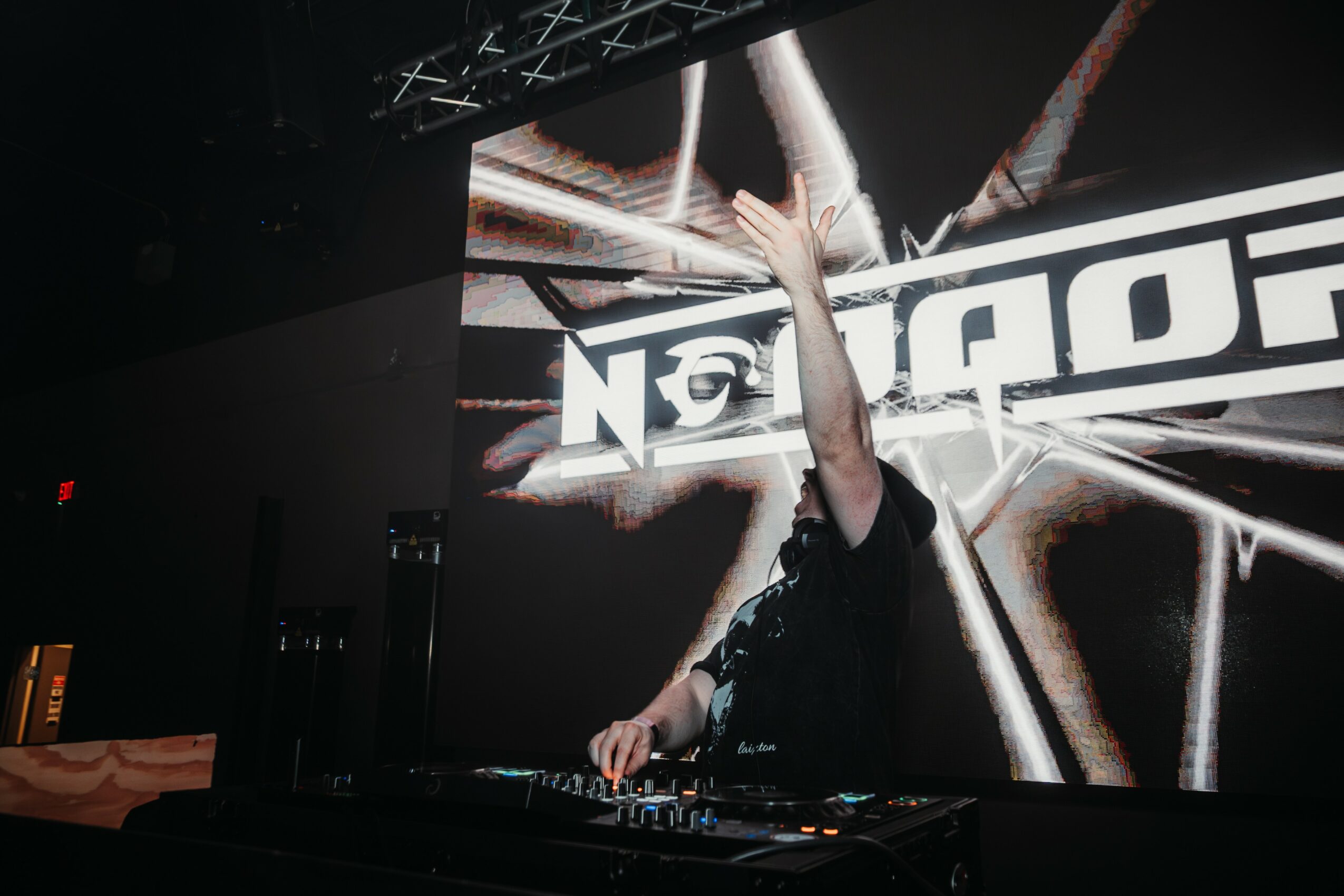Person with raised arm performing on stage with a large screen displaying graphics behind them.