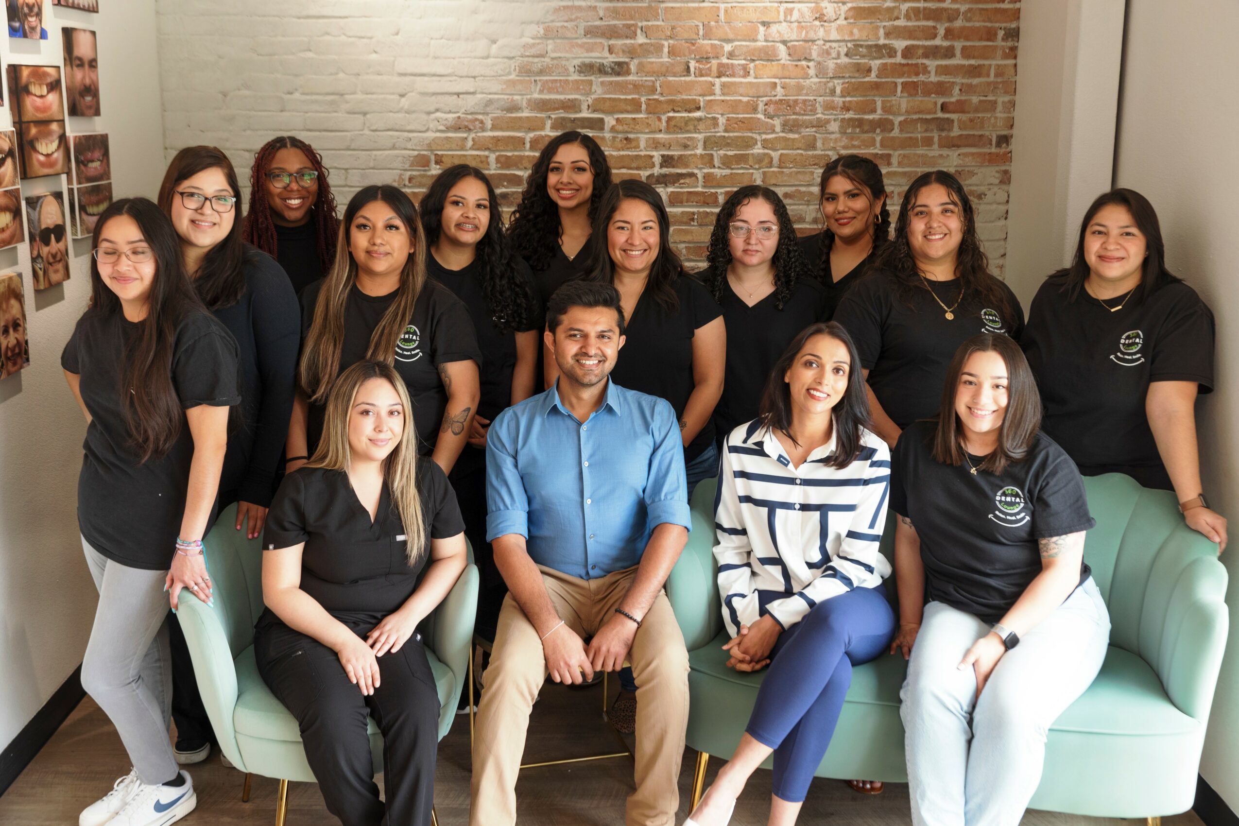 Group of fifteen people, mostly women, standing and sitting in a room with a brick wall background, smiling.