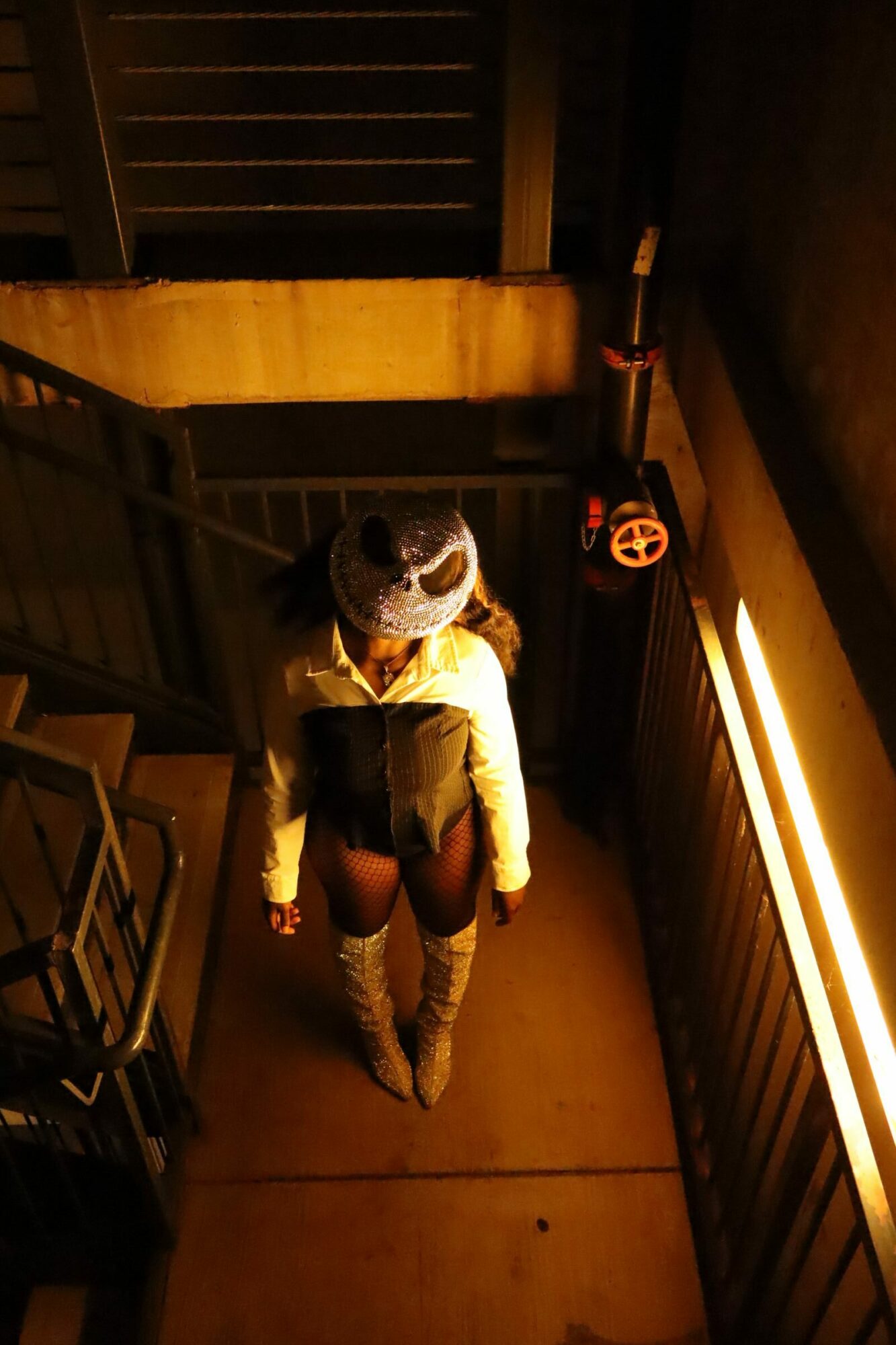 Person standing on a dimly lit outdoor staircase at night, holding a bag, with a railing and stairs visible.