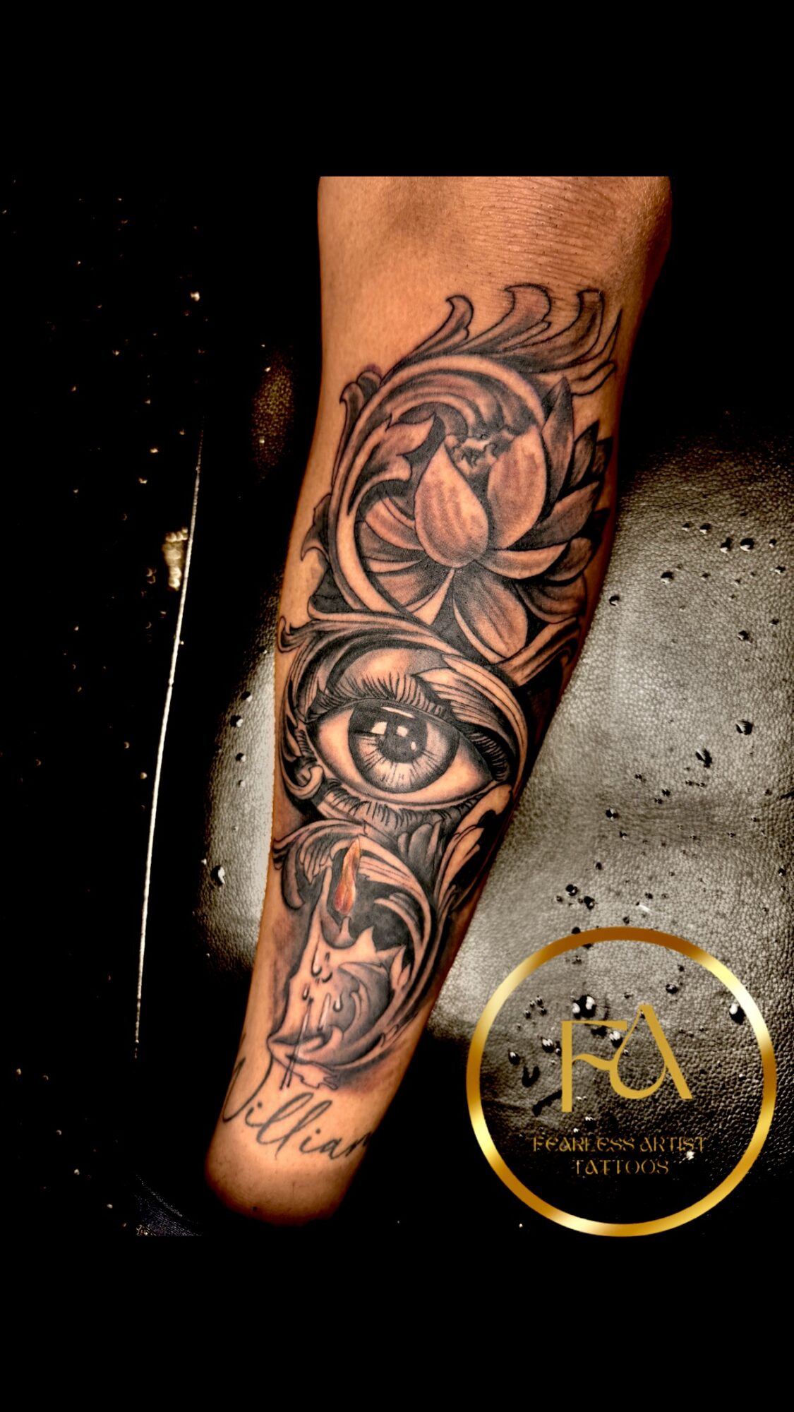 Tattoo of a lotus flower, eye, and decorative patterns on a person's forearm, with a dark background.