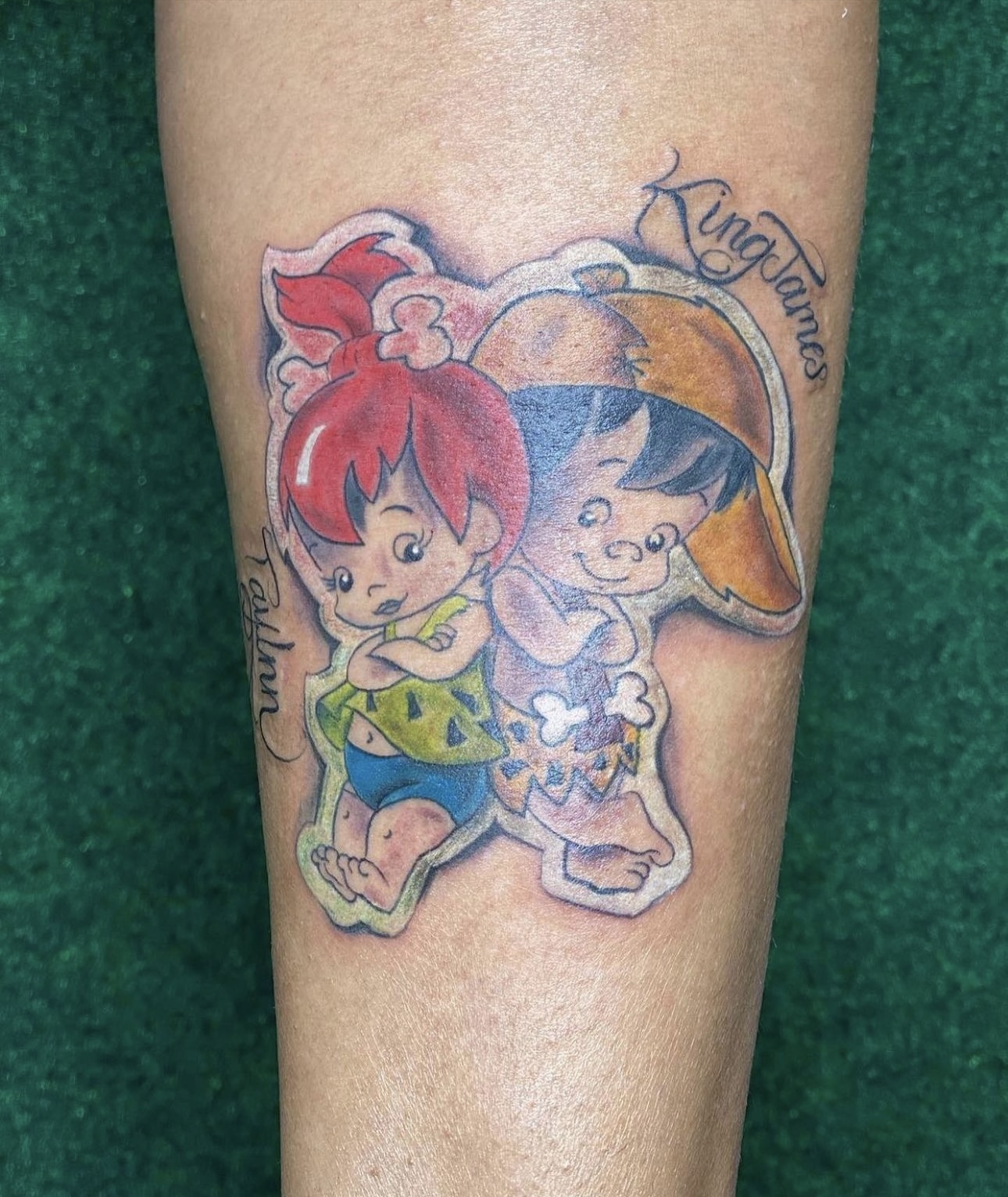 Colorful tattoo of two cartoon characters, one with red hair and the other with black hair, with text above and below.