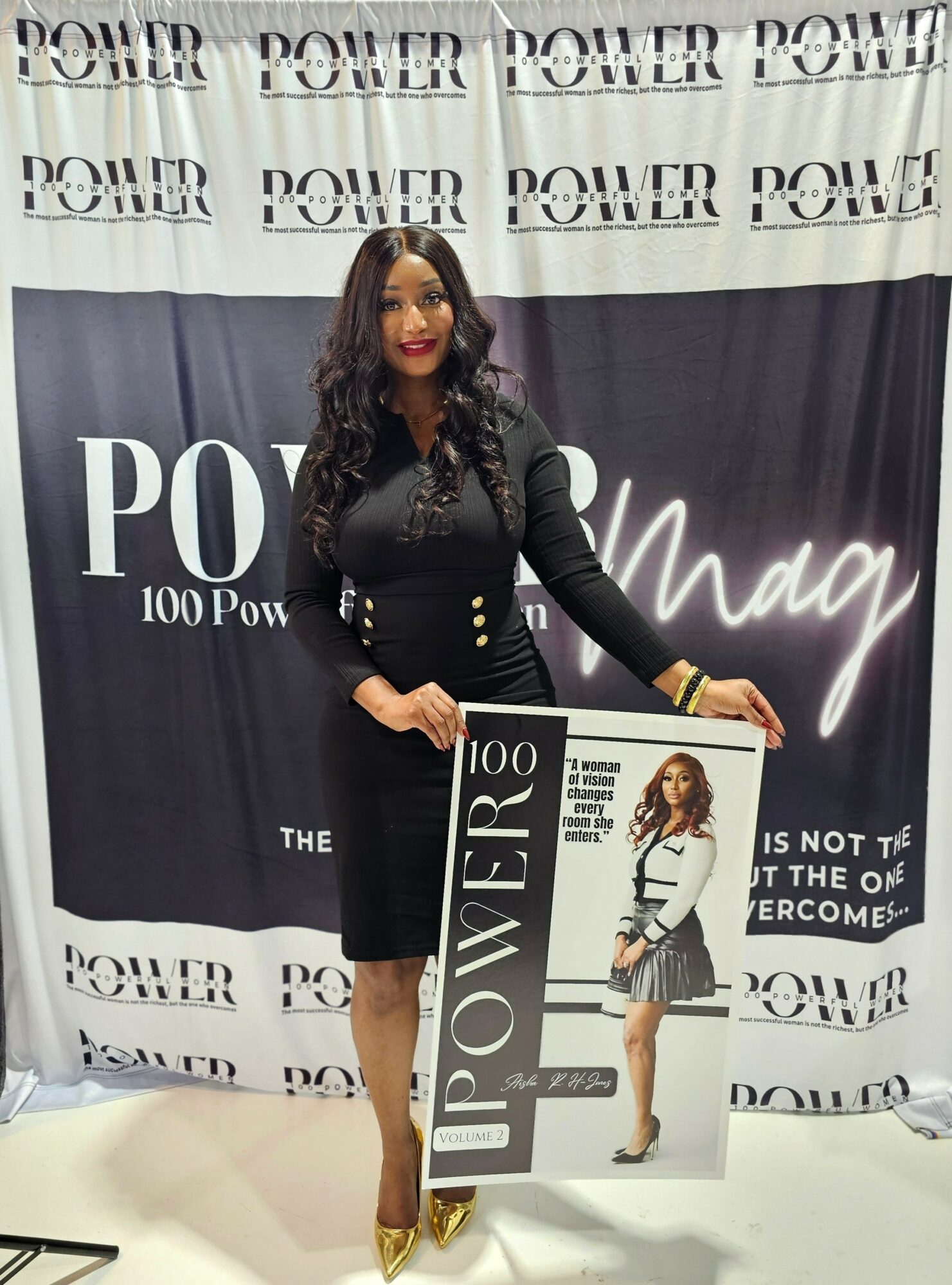 Woman in black dress holding a Power magazine, standing in front of a Power-themed backdrop with text and logo, smiling.
