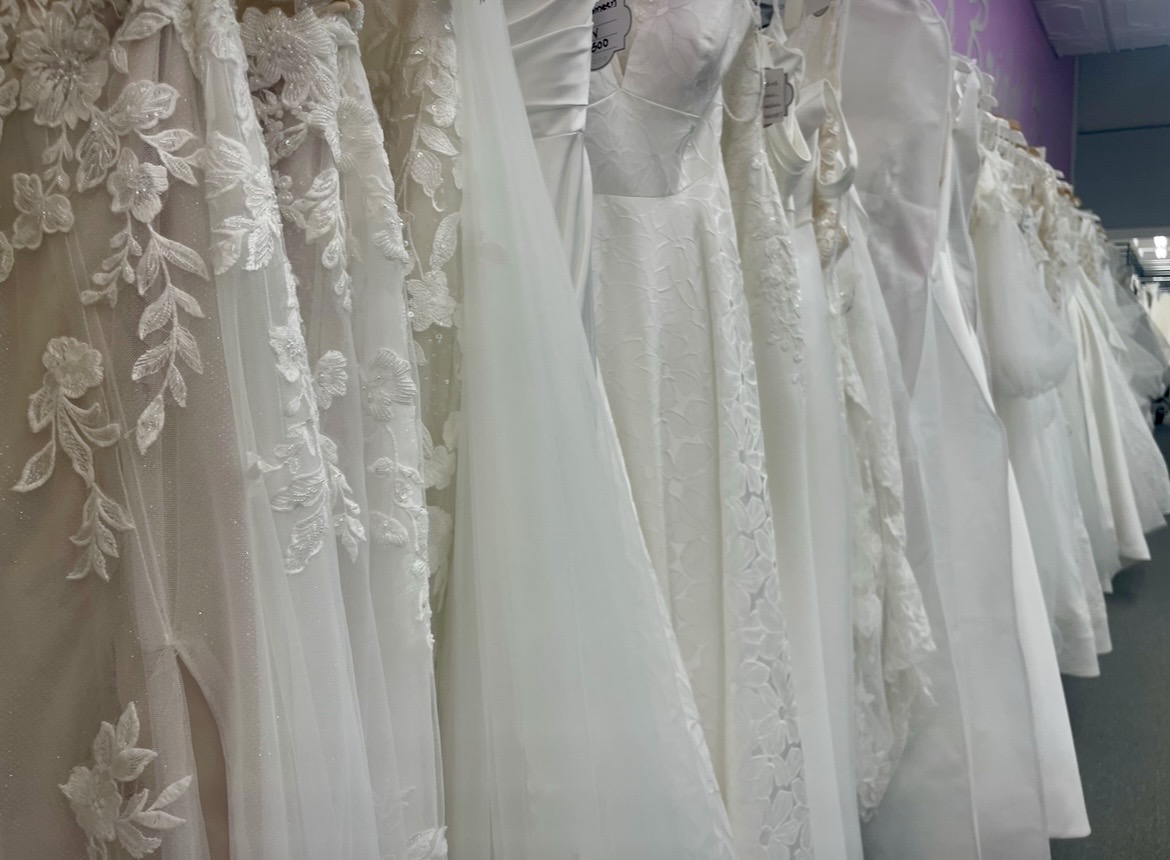 Wedding dresses hanging on a rack, featuring lace, embroidery, and satin fabrics, in a bridal store.