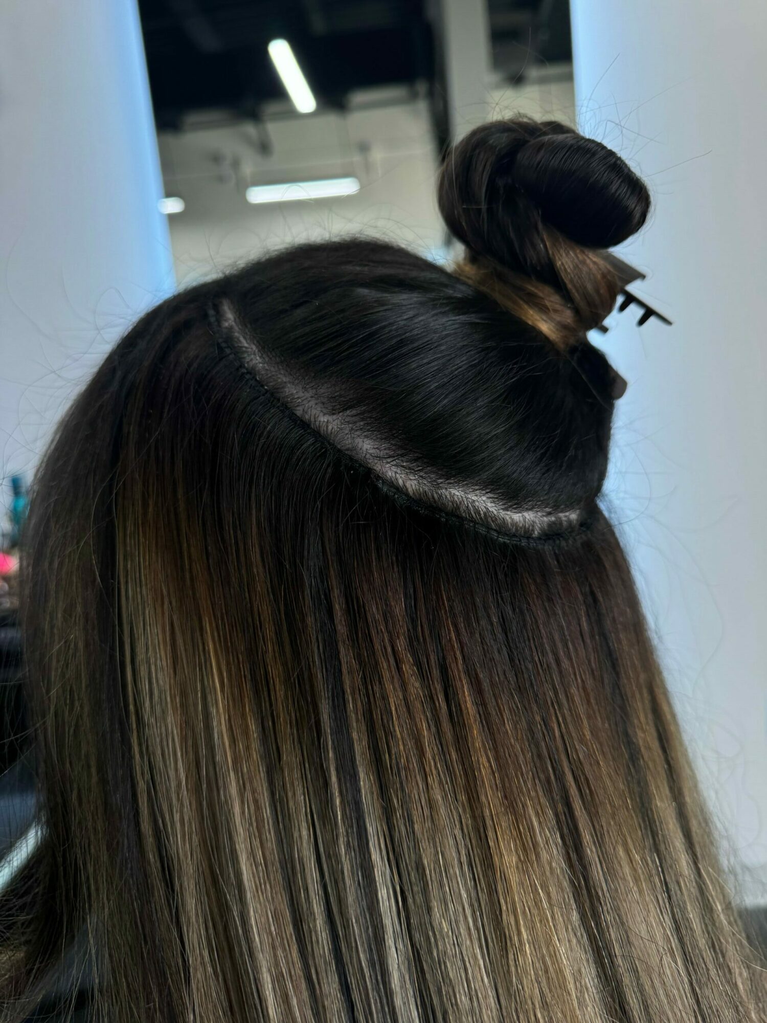 Top view of a person's head with long, straight hair and a hair bun secured with a hair clip.