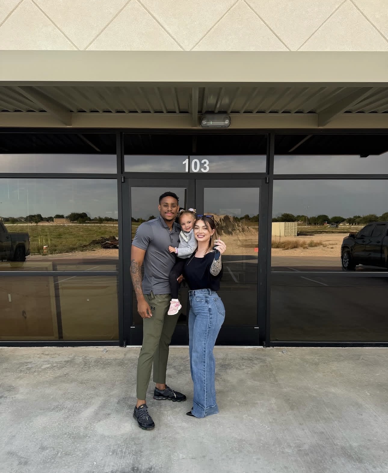 Three people standing outside a building with glass doors, number 103, smiling and posing for a photo.