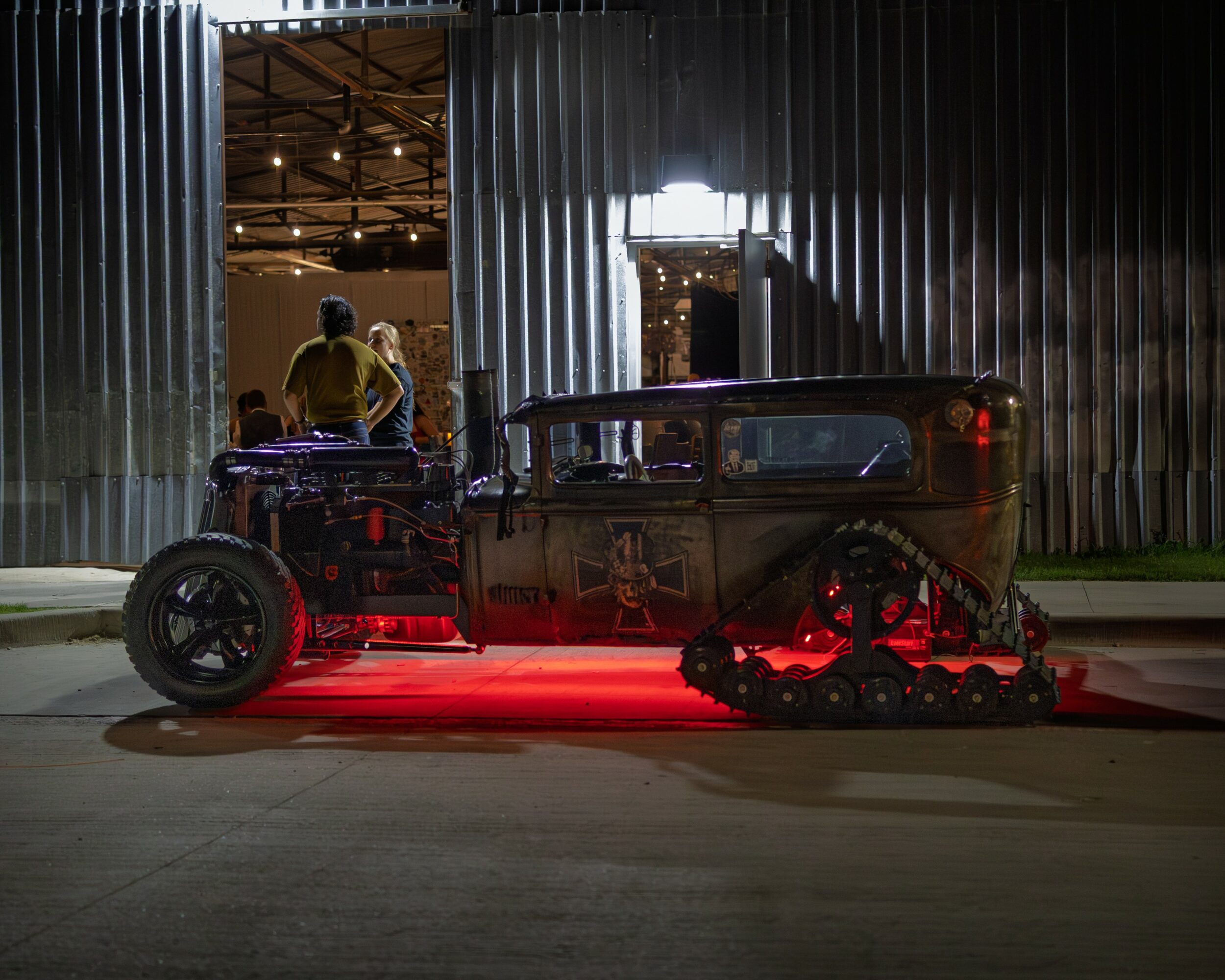 Vintage car with tank tracks and red underglow lights parked outside a building at night.