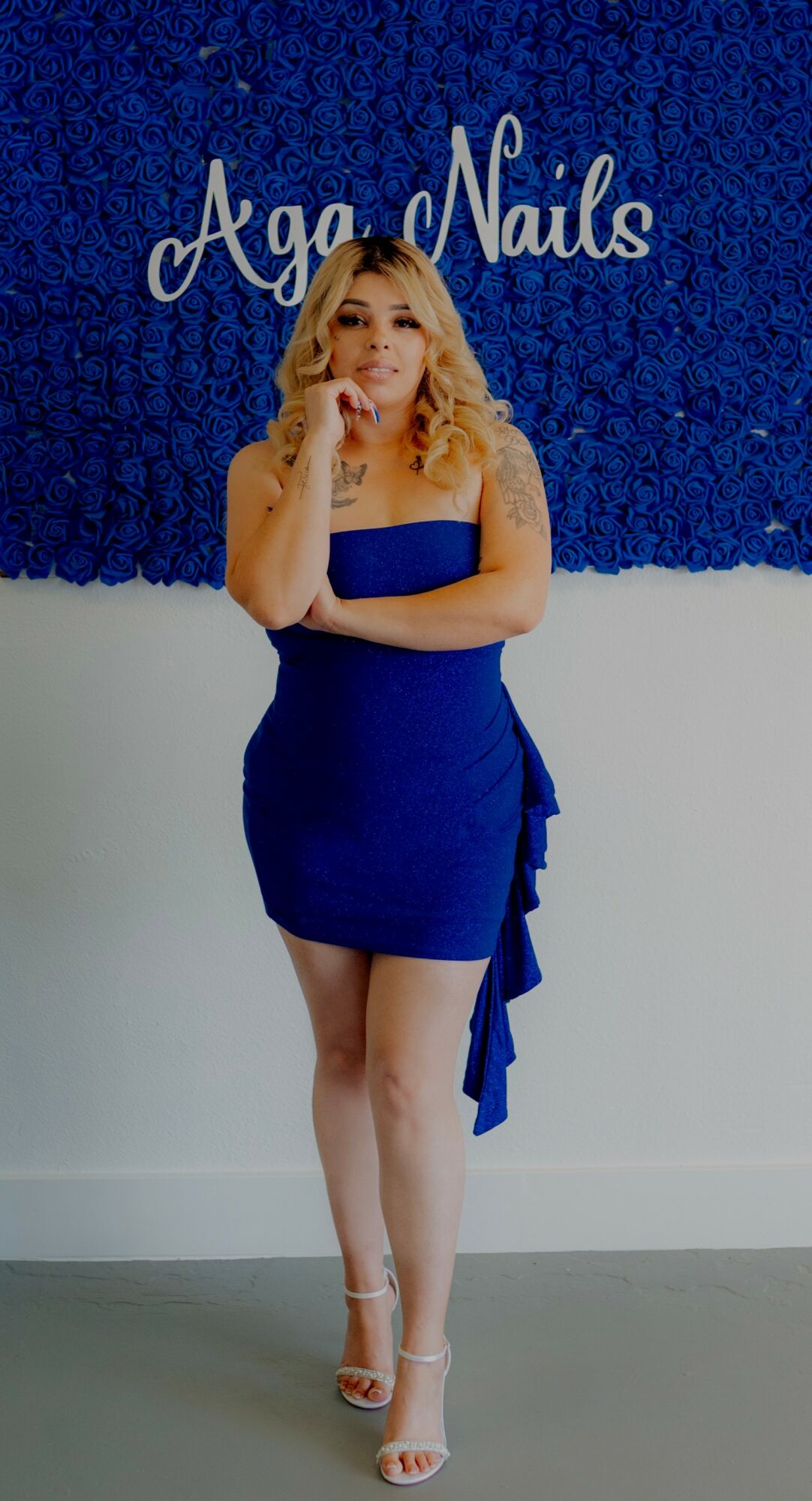 Woman in blue dress standing in front of a sign that reads 'Aga Nails'.