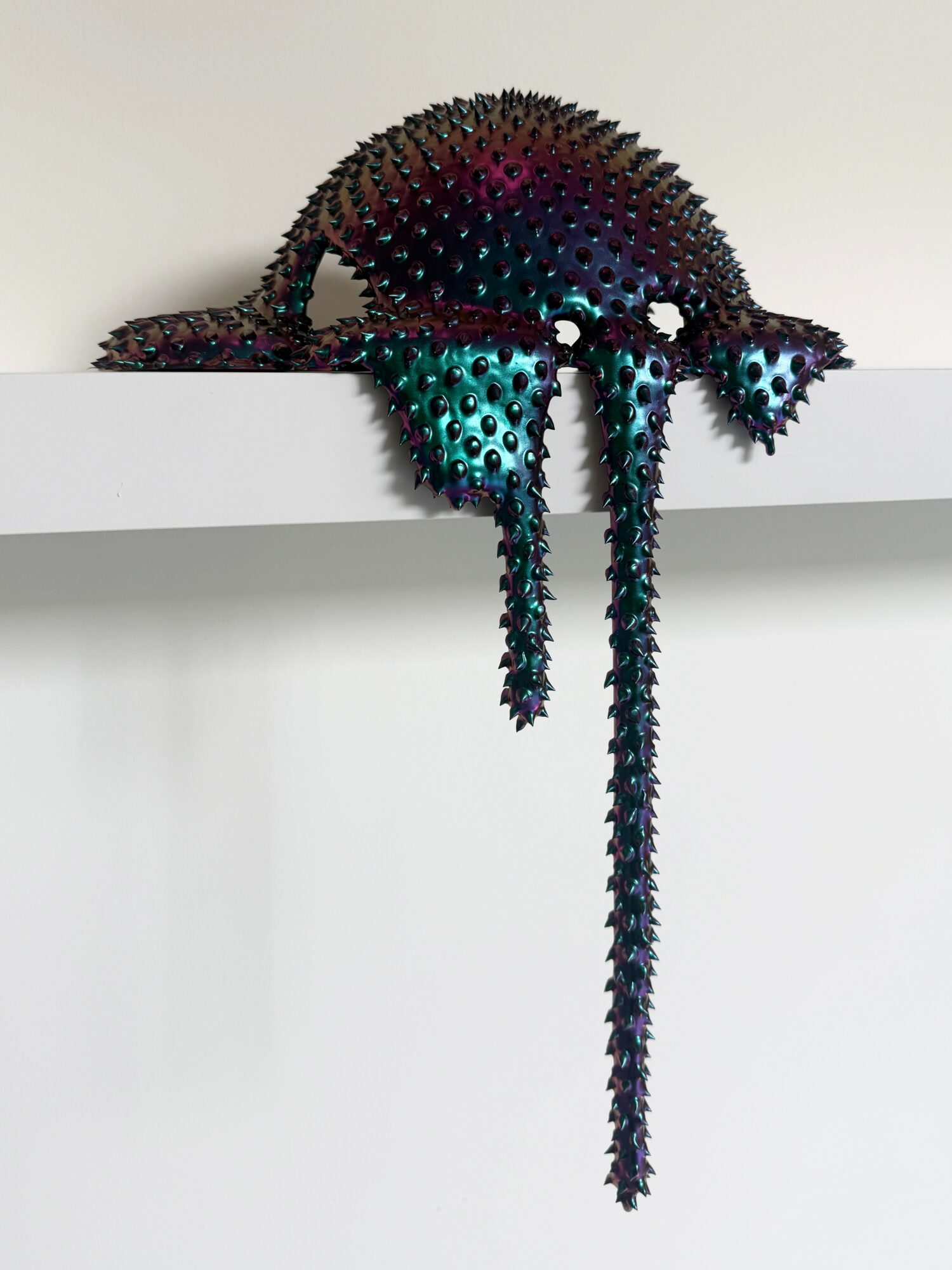 Colorful chameleon sculpture with spiky texture resting on a white shelf.