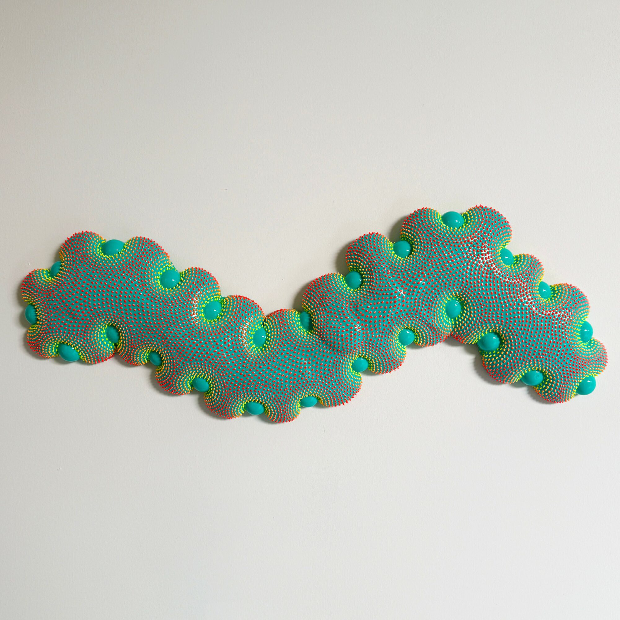 Colorful textured object with rounded bumps, shaped like a wavy line, on a plain white background.
