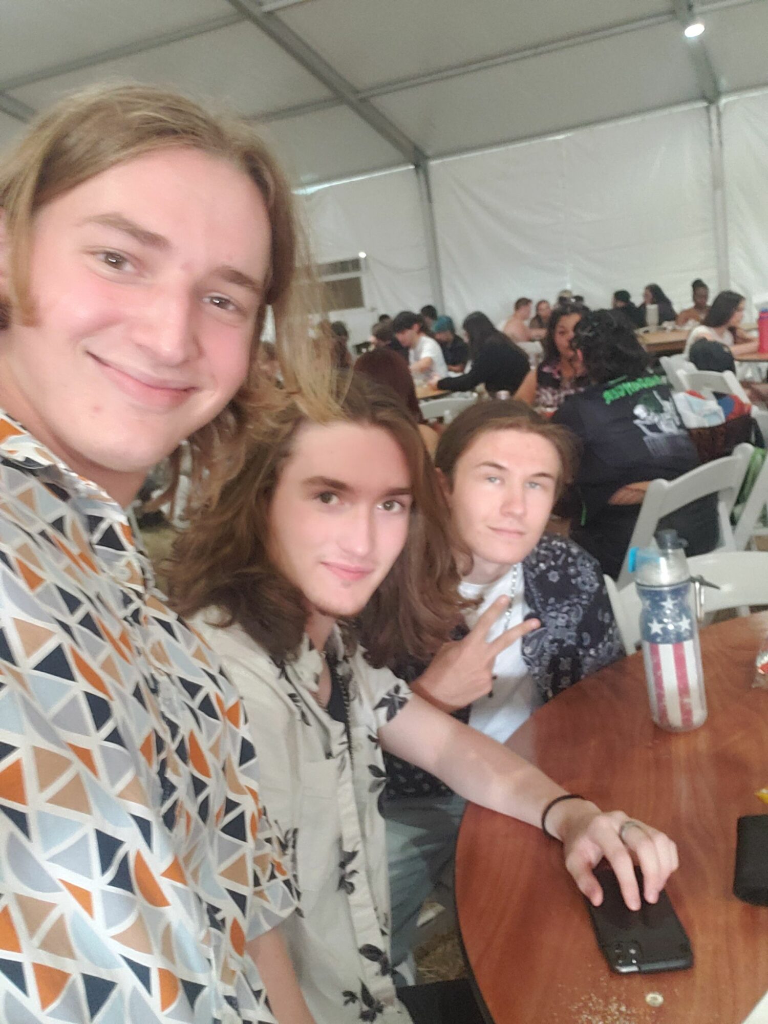 Three women taking a selfie at a table in a crowded indoor event, smiling and posing for the camera.