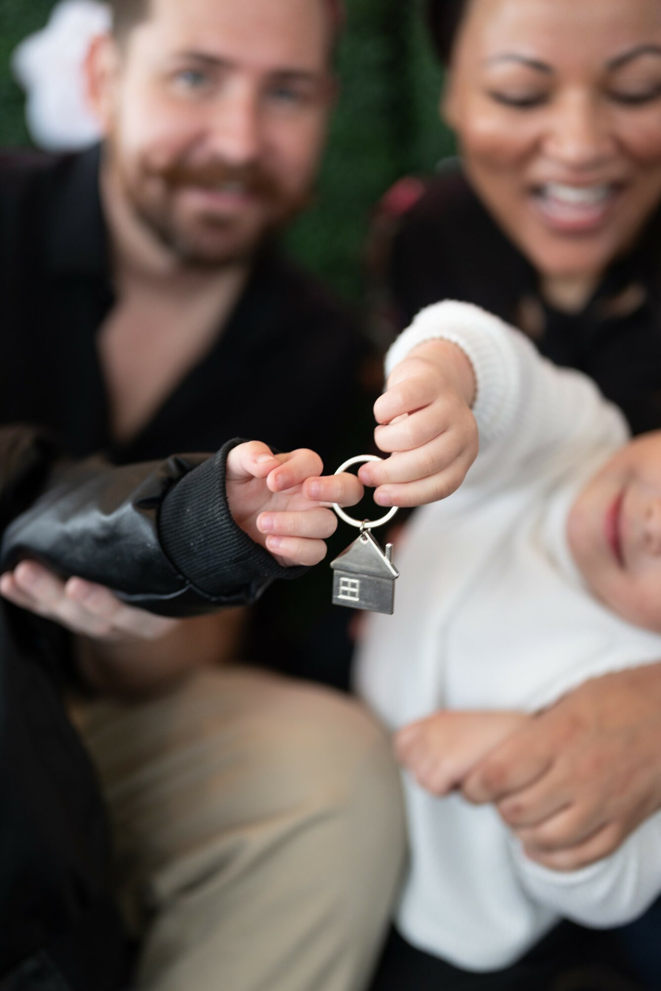Two adults and a child holding a keychain with a house charm, smiling outdoors.