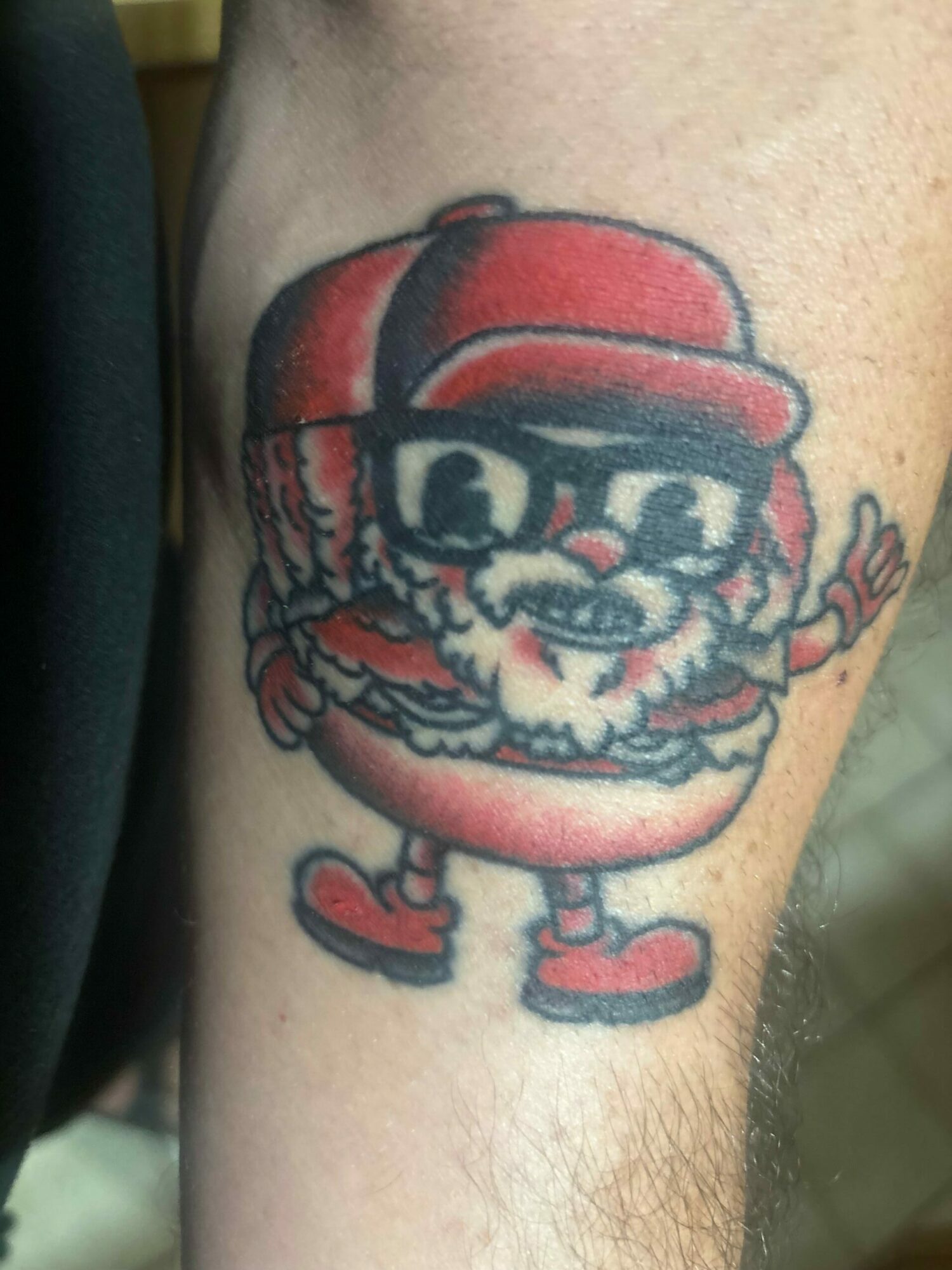 Tattoo of a cartoon character with a red hat and a large red object, on a person's arm.