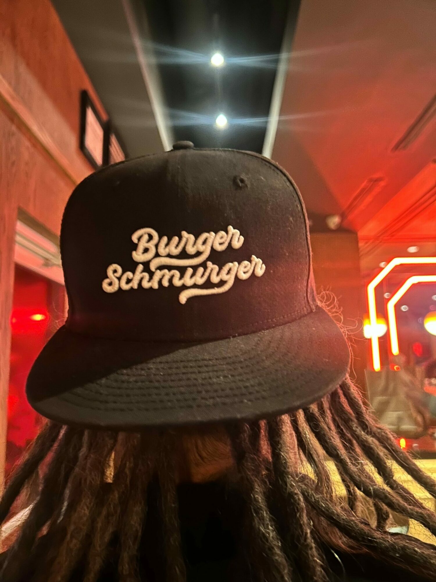 Black cap with white embroidered text reading 'Beverly Schweyzer' on the front, worn by a person with long dreadlocks.