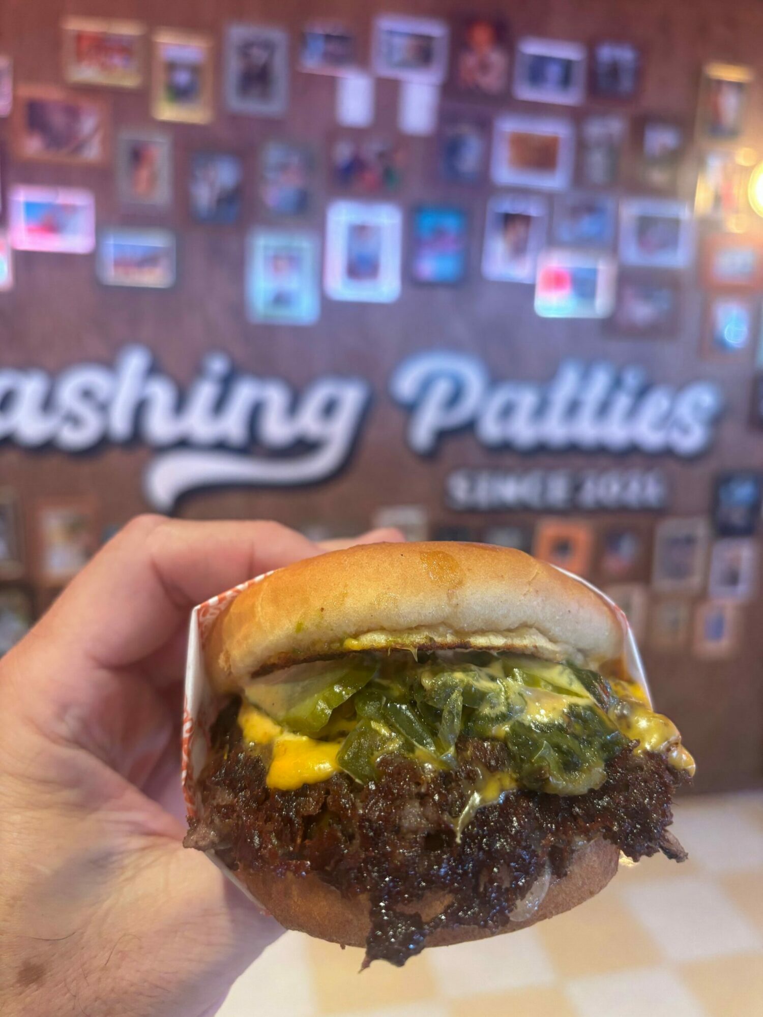 Hand holding a burger with lettuce, cheese, and a beef patty, against a blurred background with text and images.