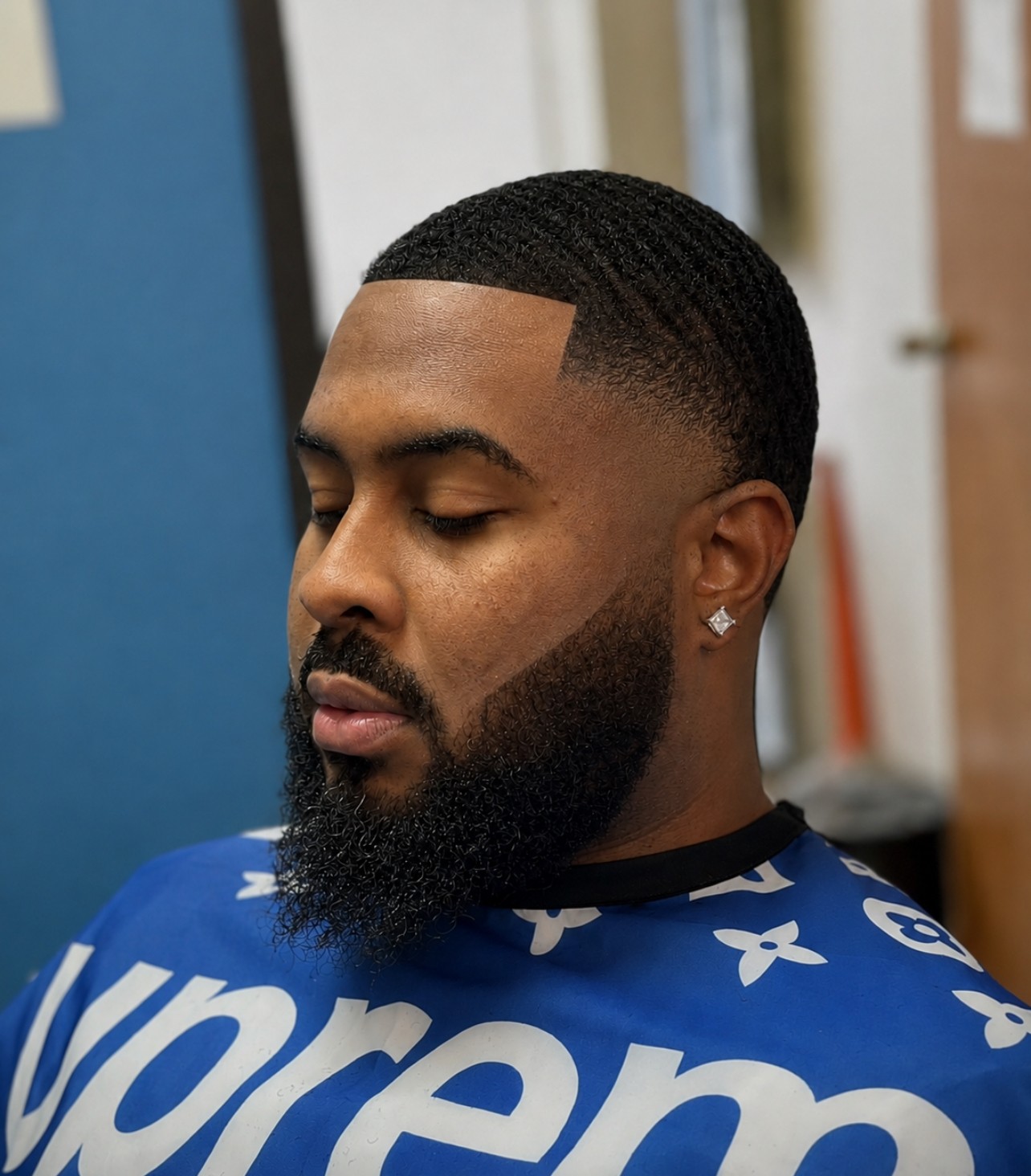 Man with a beard and short hair, wearing a blue sports jersey, looking down, in an indoor setting.
