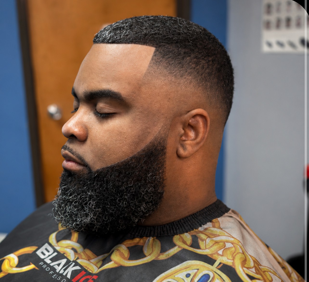 Side profile of a man with a fade haircut and full beard, eyes closed, in a barbershop chair.