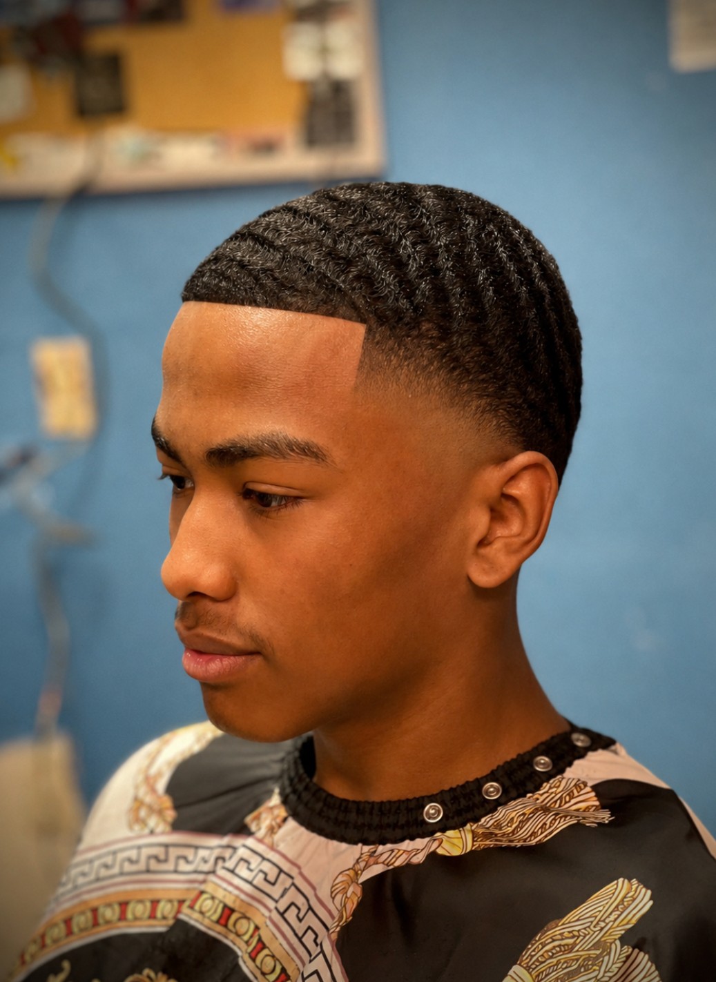 Young man with a short, textured haircut looking to the side, indoors with a blue wall background.