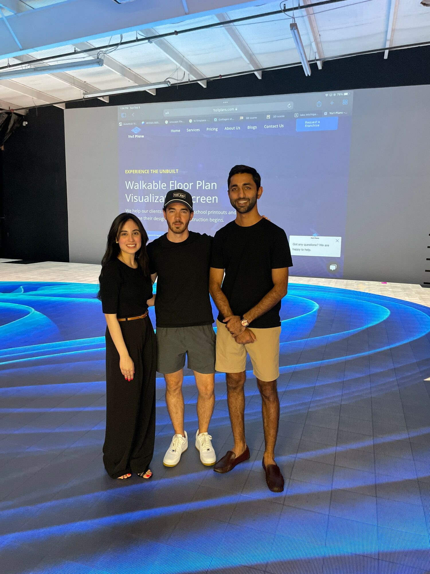 Three people standing in front of a large screen with blue circular patterns, smiling, in a modern indoor setting.